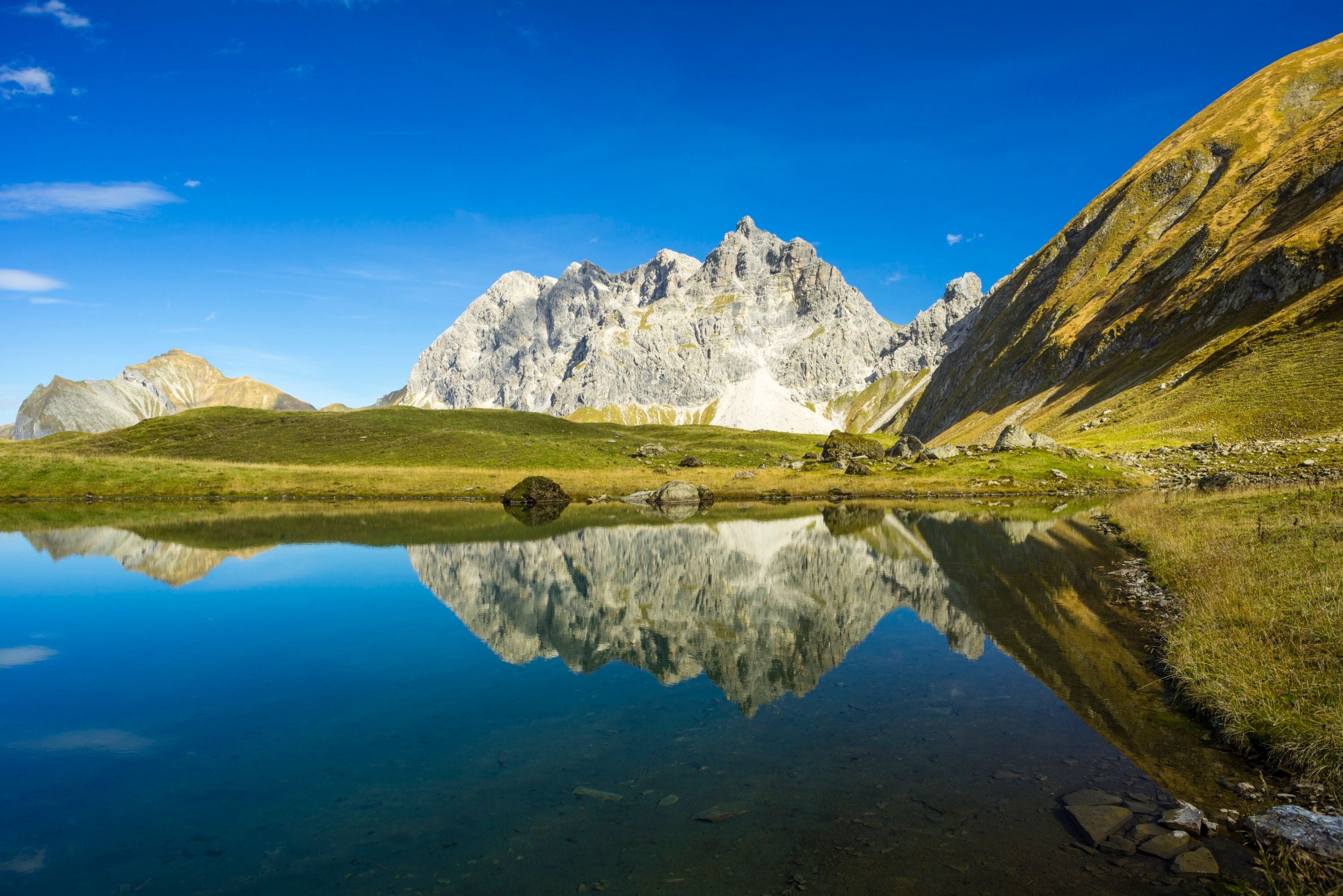 Klarer Bergsee mit Spiegelung der Gipfel im Oytal, Allgäuer Alpen, unter blauem Himmel.