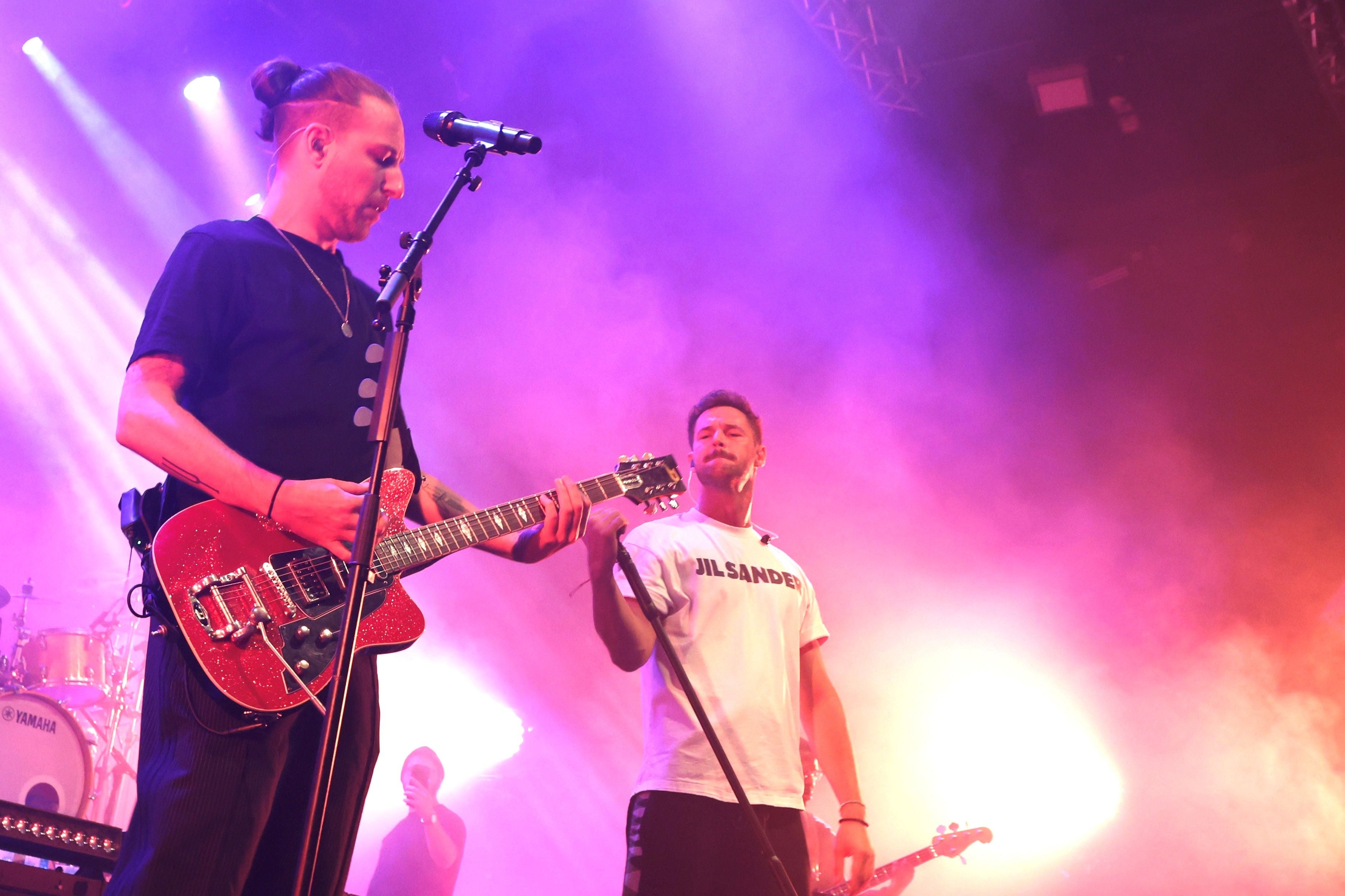 Zwei Musiker treten auf einer bunt beleuchteten Bühne mit Gitarre und Mikrofon auf.