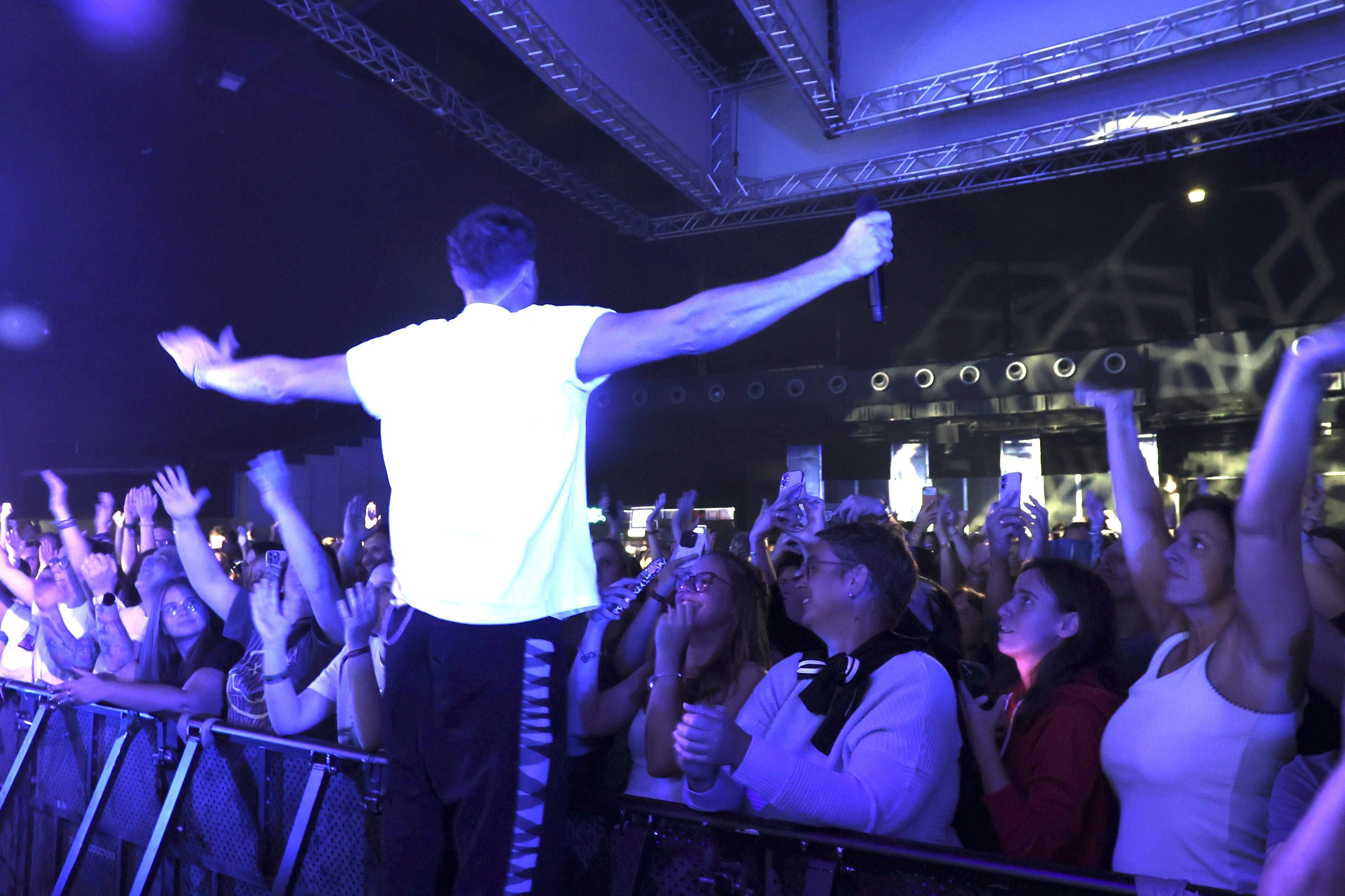 Sänger steht mit ausgebreiteten Armen vor jubelndem Publikum auf einem Konzert.