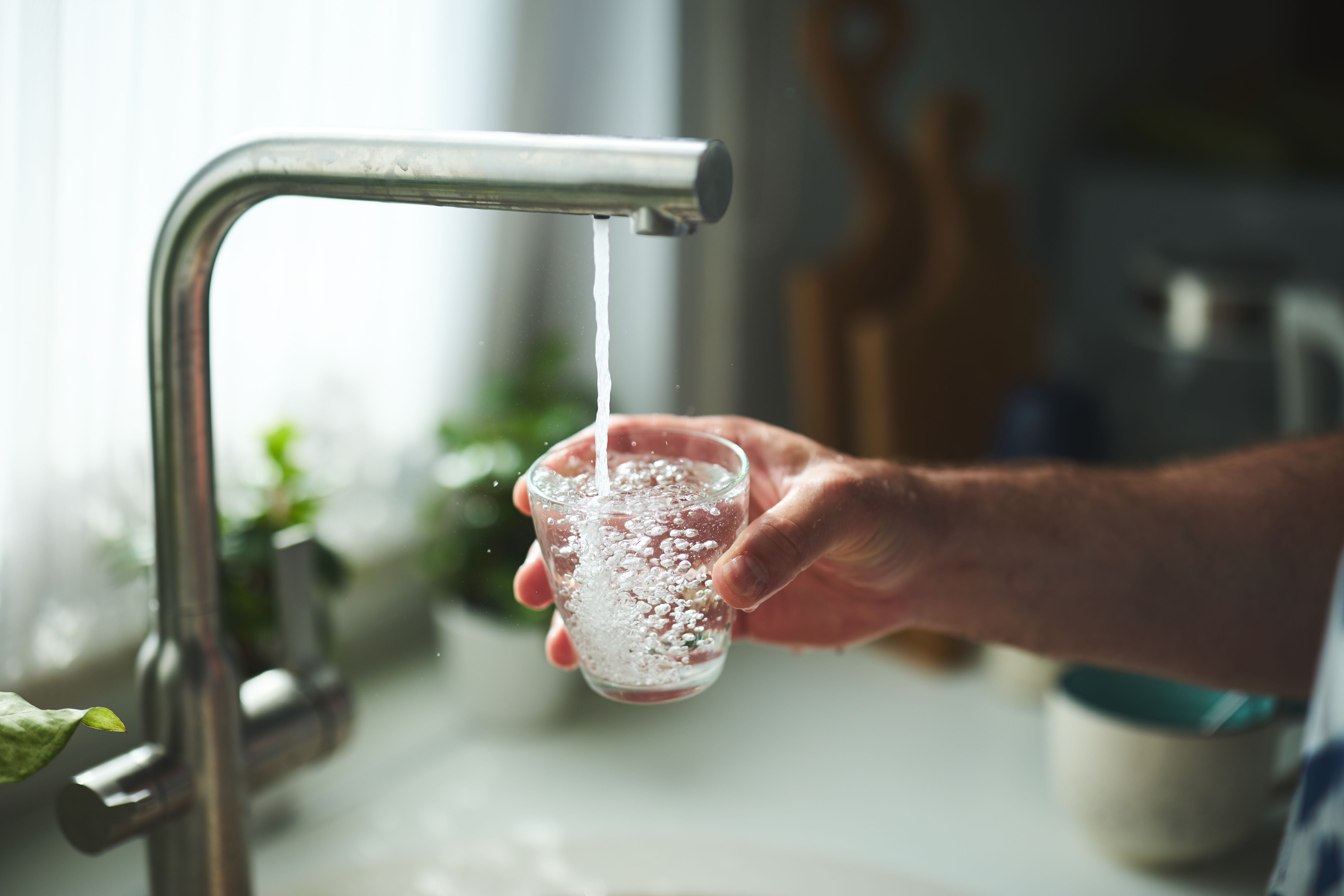 Eine Hand füllt ein Glas mit Leitungswasser an einem Küchenwasserhahn.