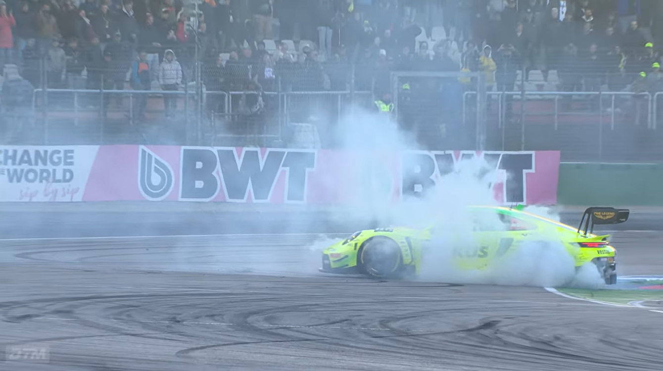ÖSV-Motorsport-Star Thomas Preining zündet im grellgelben Manthey-Porsche beim Siegesjubel auf dem Hockenheimring rauchende Donuts auf der Asphaltstrecke vor der Tribüne.