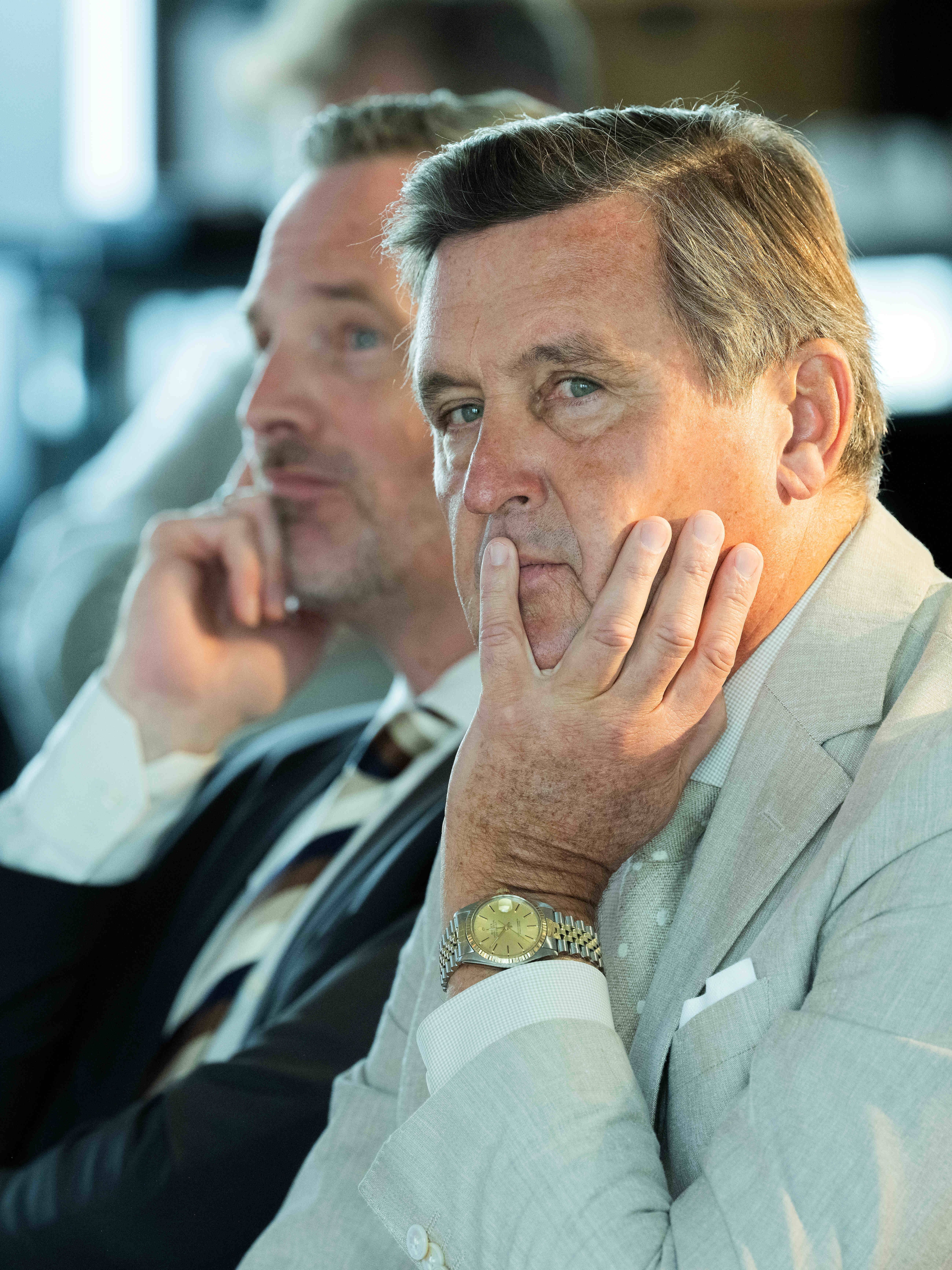 Zwei Männer im Anzug sitzen nachdenklich während einer Pressekonferenz.