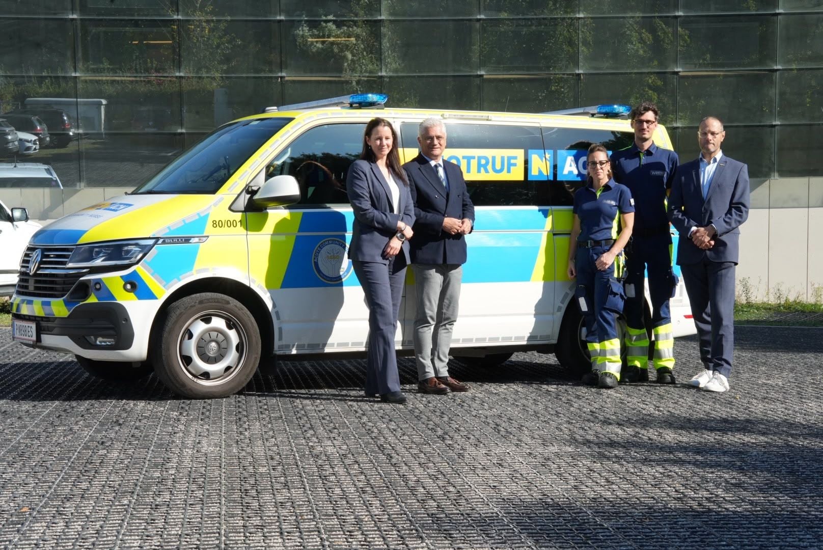 Fünf Personen stehen vor einem Notarzt-Einsatzfahrzeug im Freien.