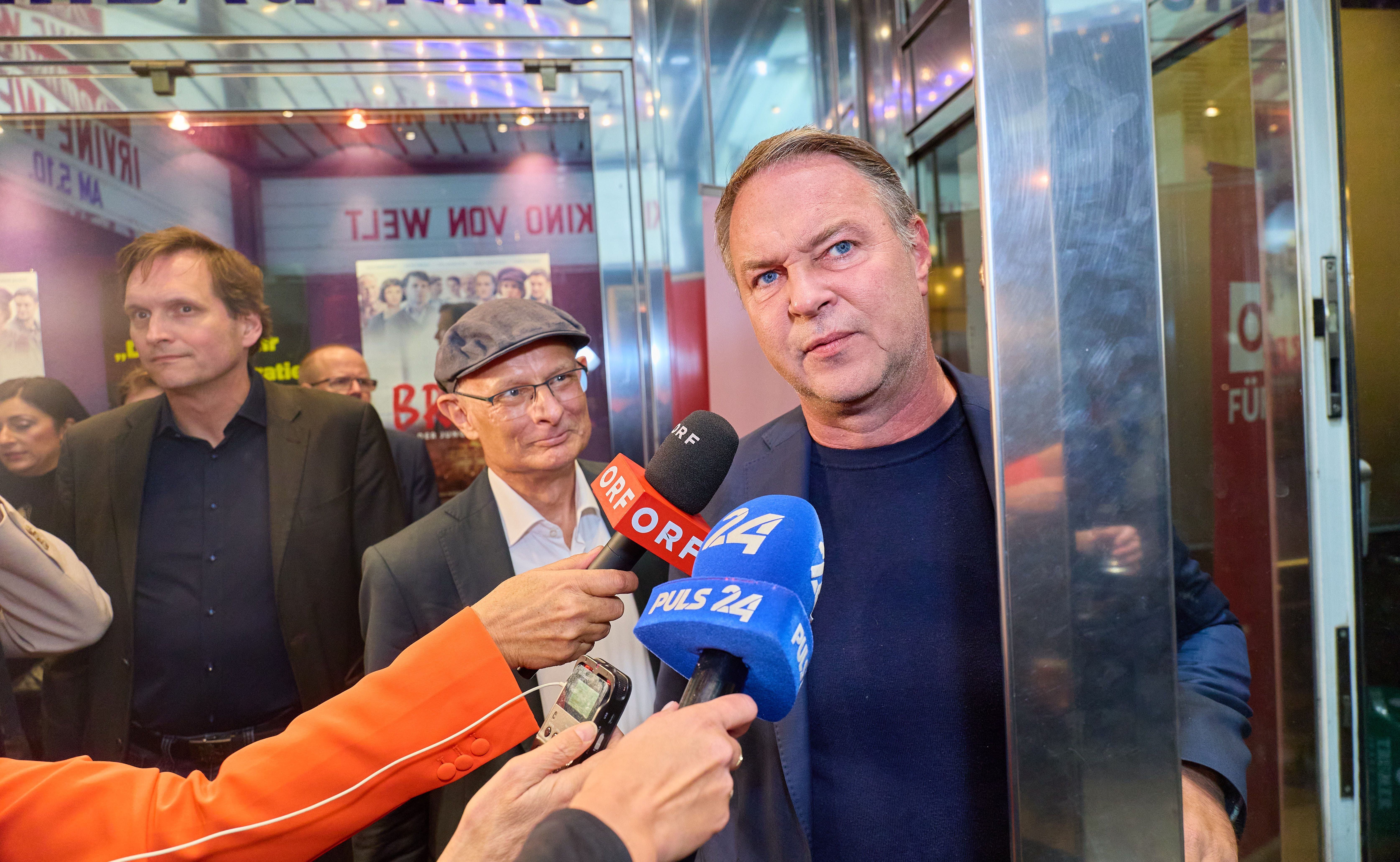 Mehrere Männer werden bei einer Premiere von Reportern mit Mikrofonen interviewt.