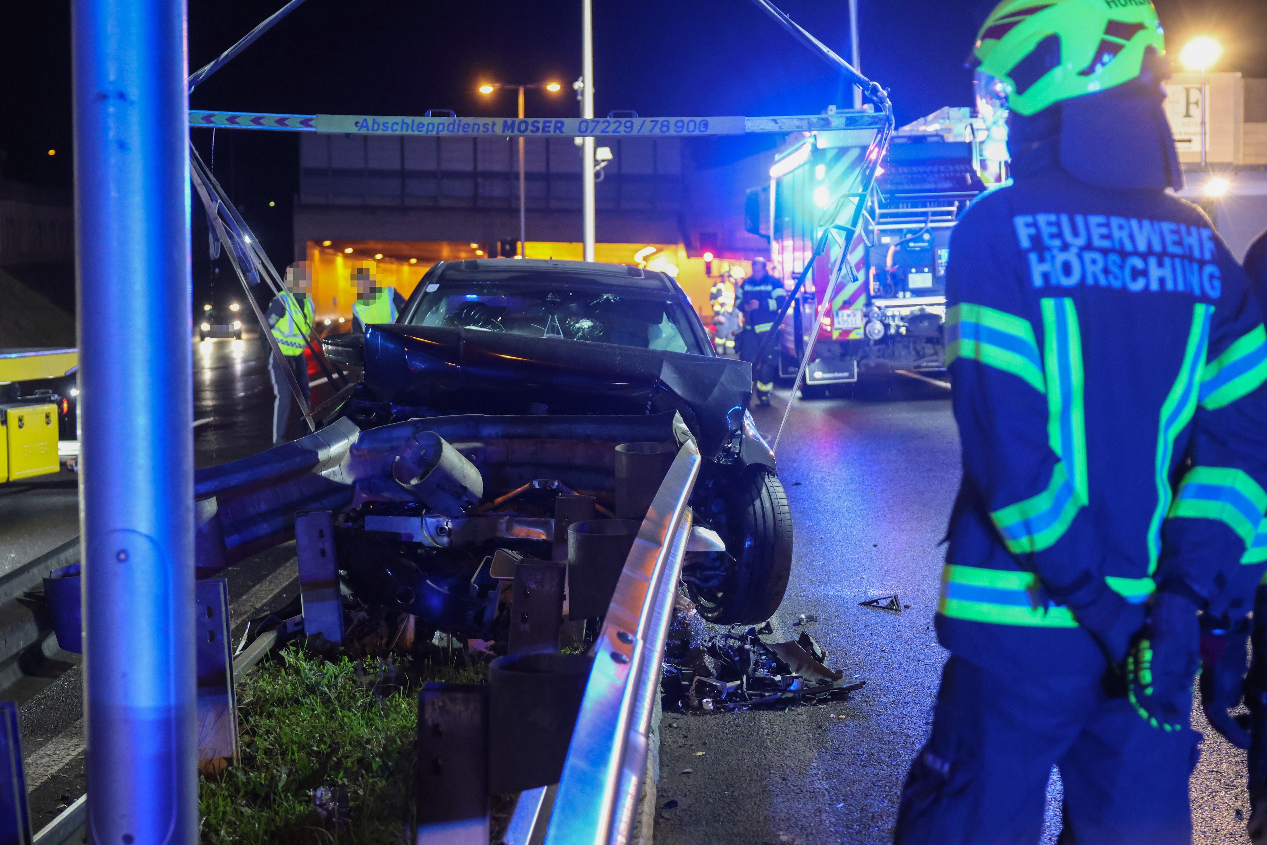 Ein Feuerwehrmann steht bei Nacht an einer Unfallstelle mit einem stark beschädigten Auto.