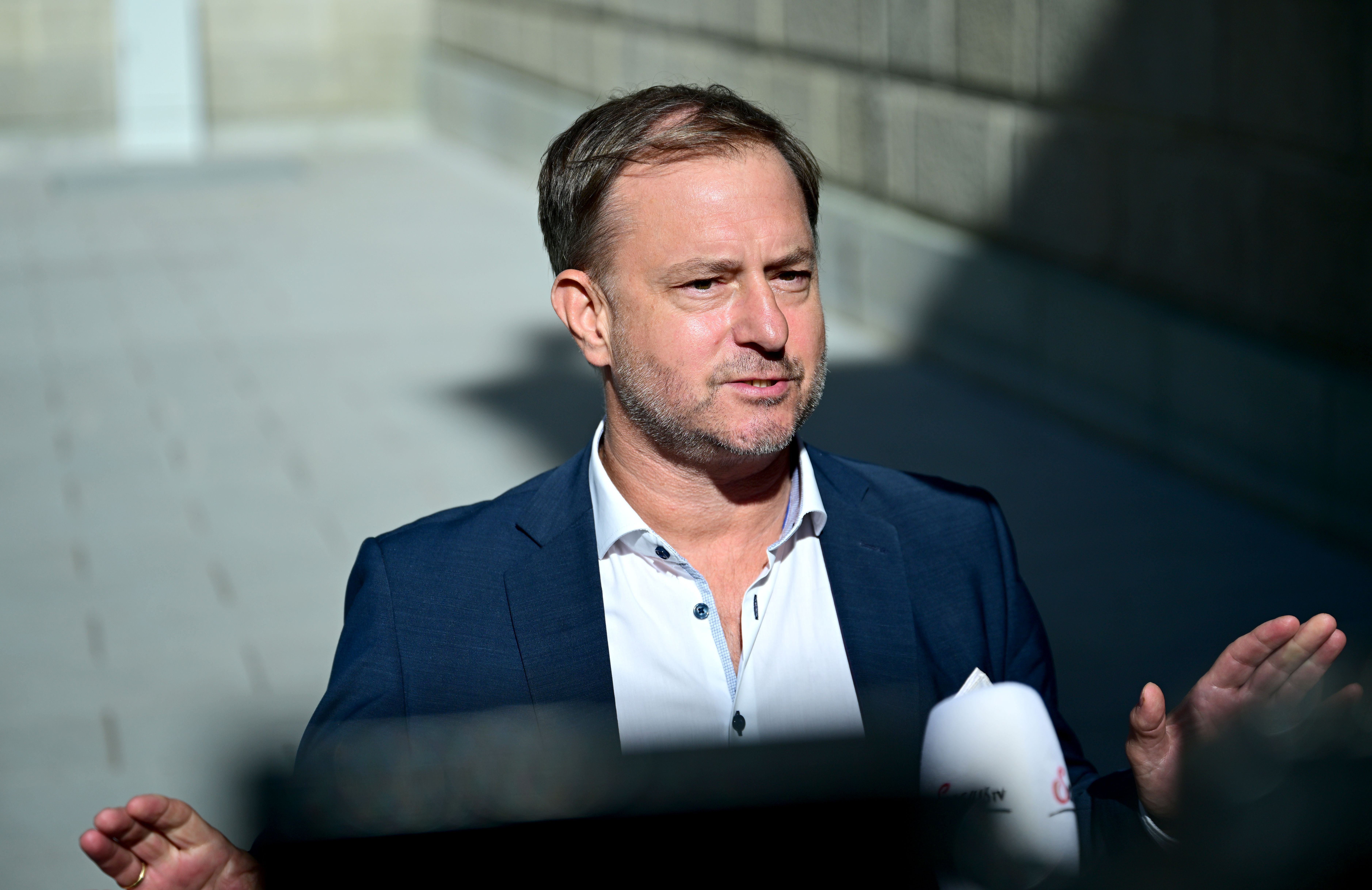 Ein Mann im Anzug spricht im Freien und gestikuliert mit den Händen.