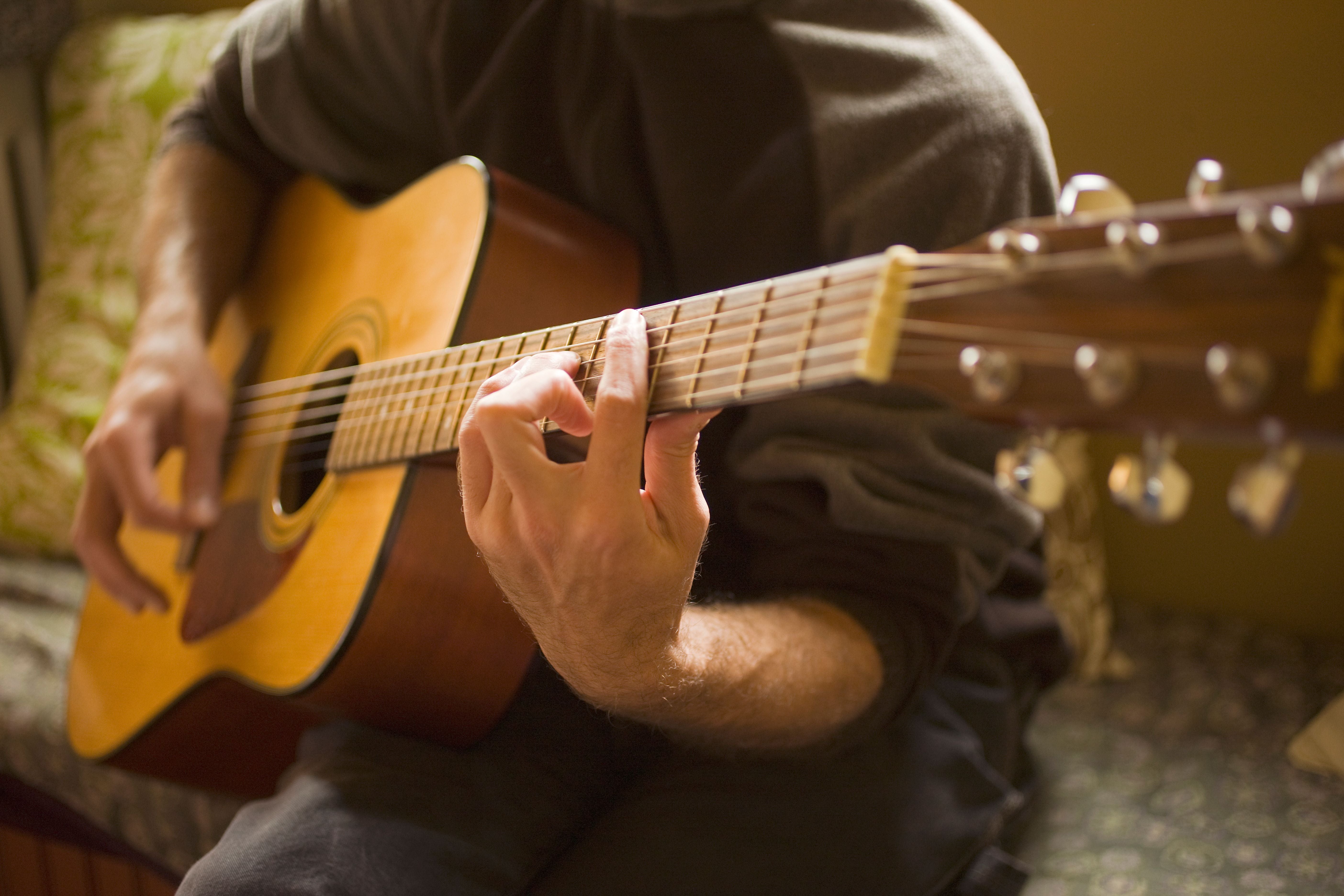 Eine Person spielt eine akustische Gitarre und greift Akkorde auf dem Griffbrett.