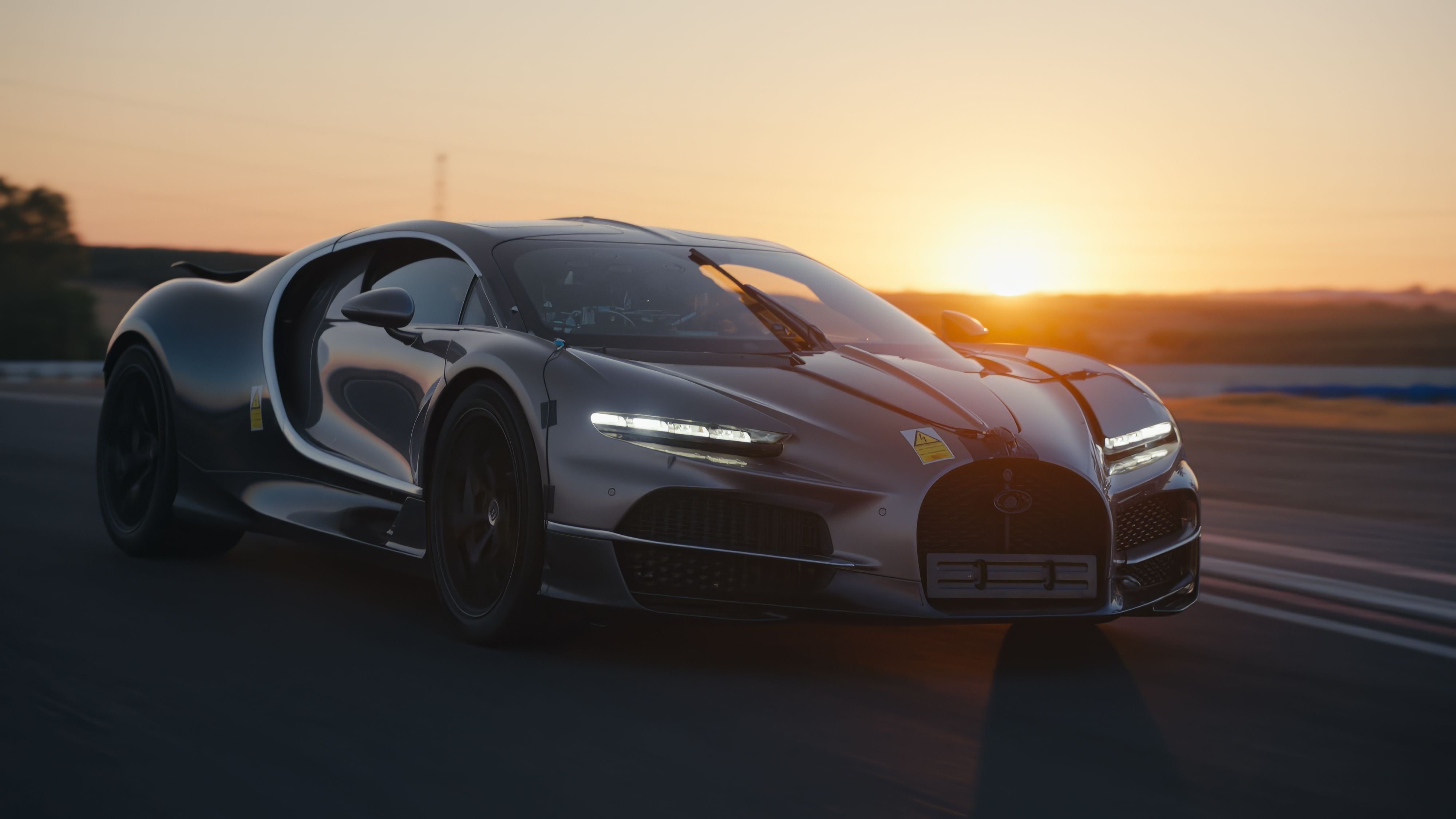 Ein schwarzer Bugatti Tourbillon fährt bei Sonnenuntergang auf einer Rennstrecke.