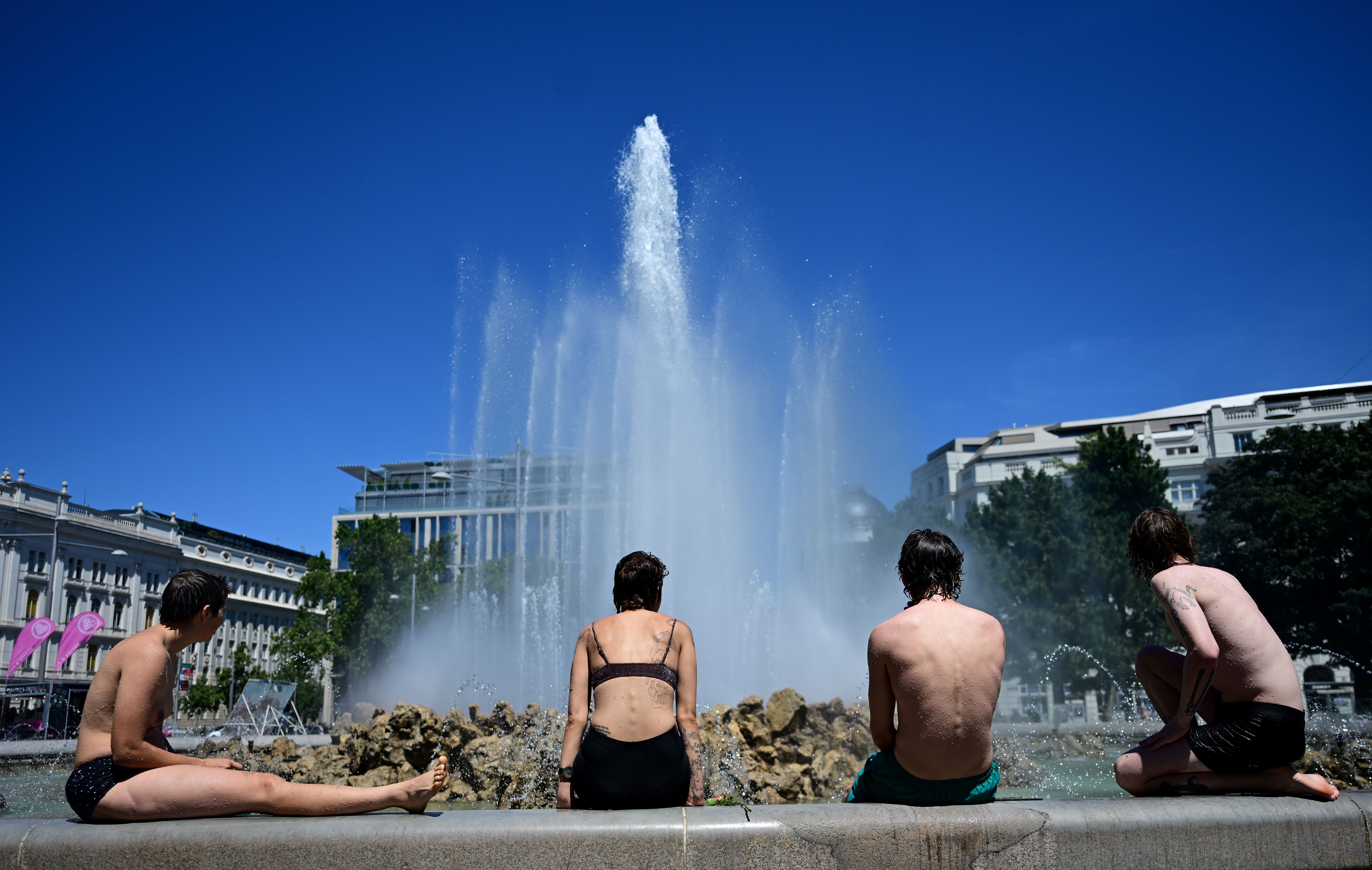 Vier junge Menschen kühlen sich bei Hitze am Hochstrahlbrunnen in Wien ab.