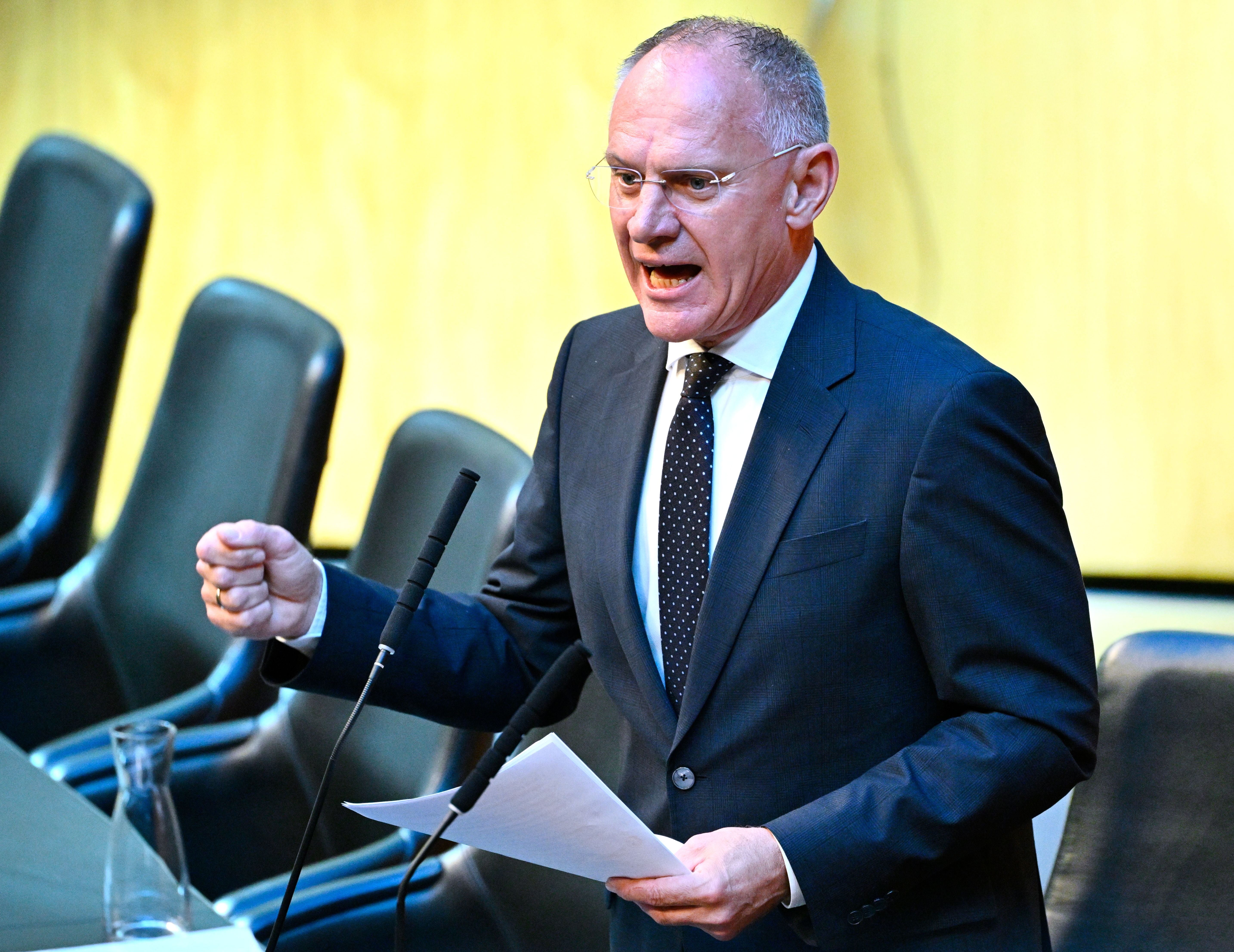 Ein Mann im Anzug spricht gestikulierend in einem Parlament am Rednerpult.