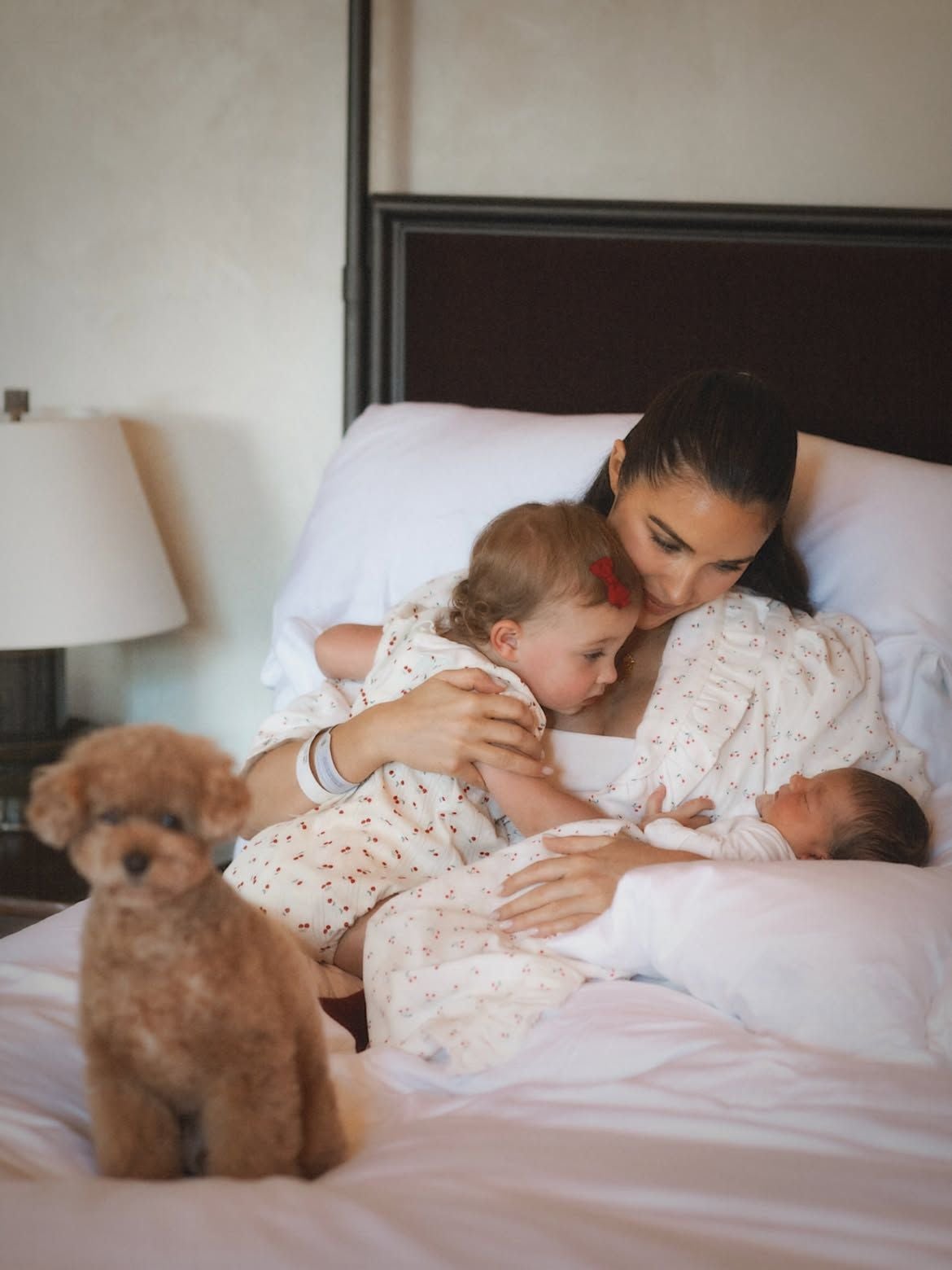 Eine Frau mit zwei kleinen Kindern und einem Hund sitzt auf einem Bett.