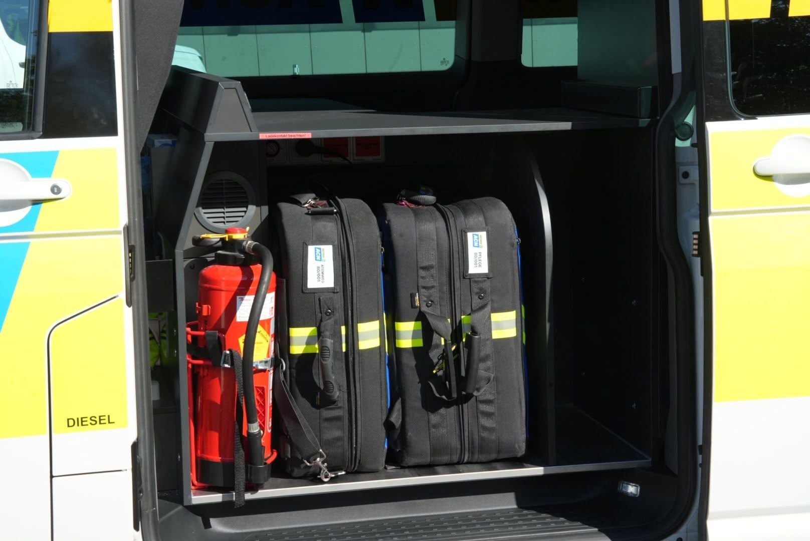 Ein offenes Einsatzfahrzeug zeigt einen Feuerlöscher und drei schwarze Notfalltaschen.