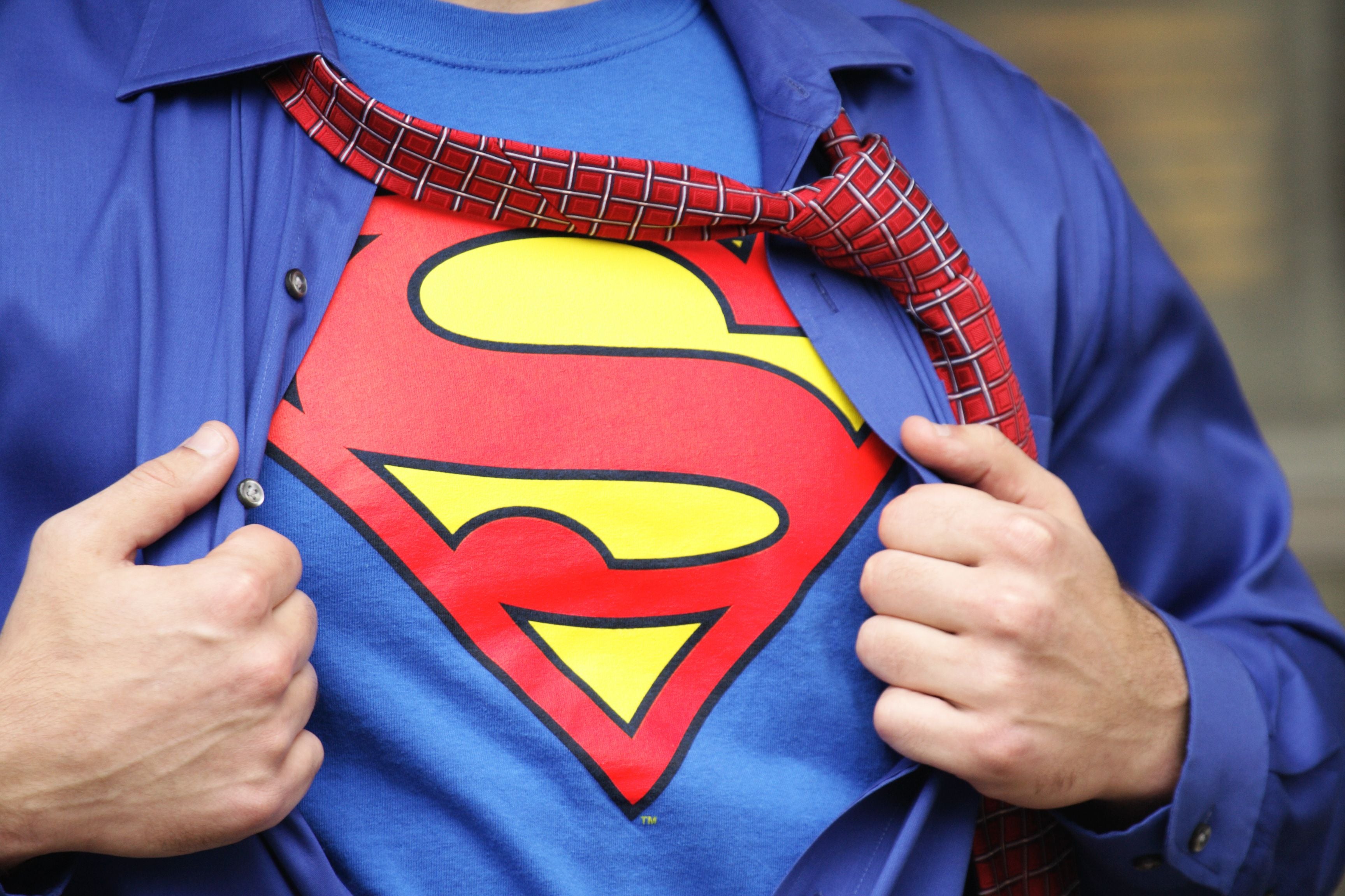 Ein Mann öffnet sein Hemd und zeigt ein Superman-T-Shirt mit rotem „S“-Logo.
