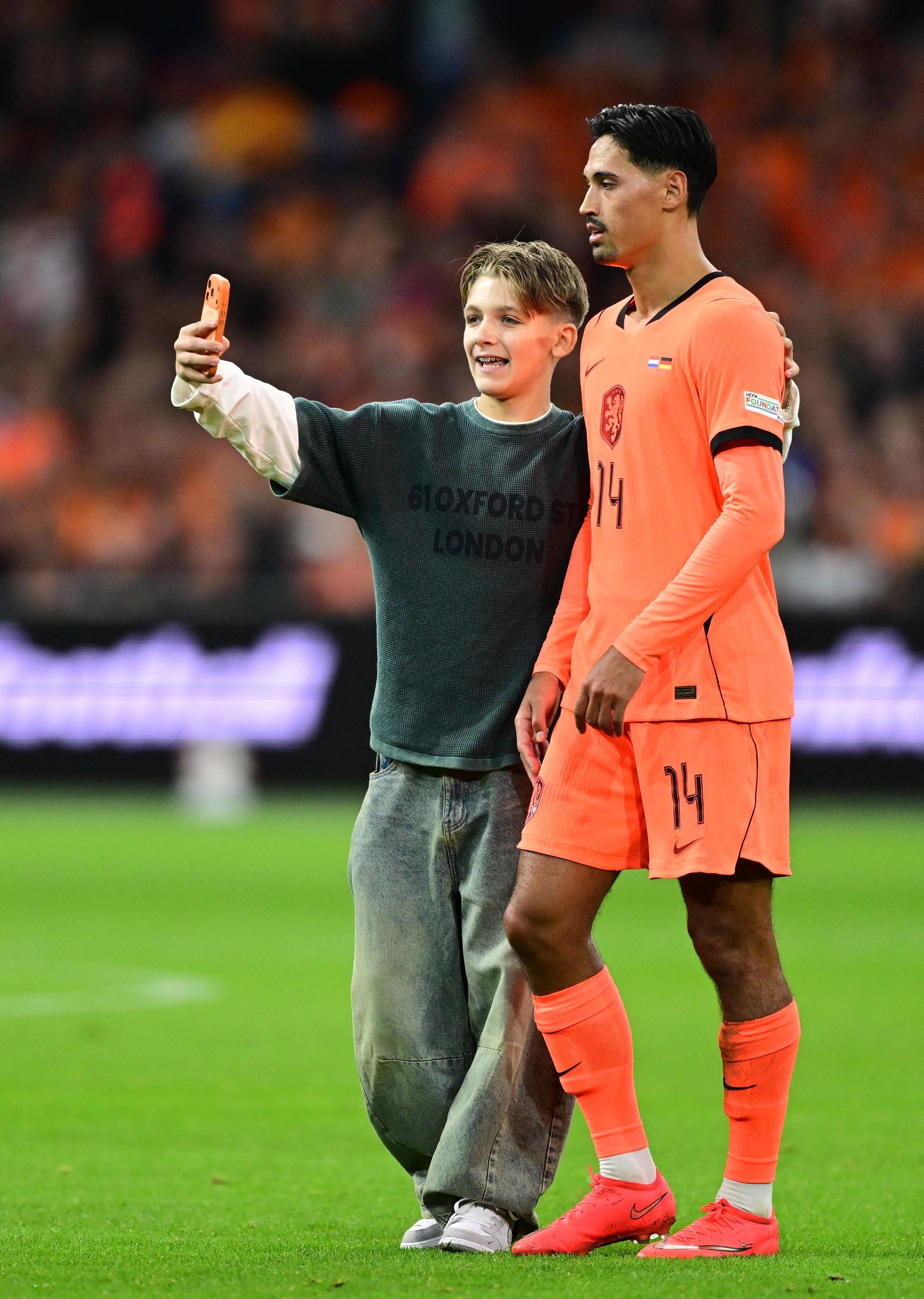 Ein junger Fan macht ein Selfie mit Fußballspieler Tijjani Reijnders auf dem Spielfeld.