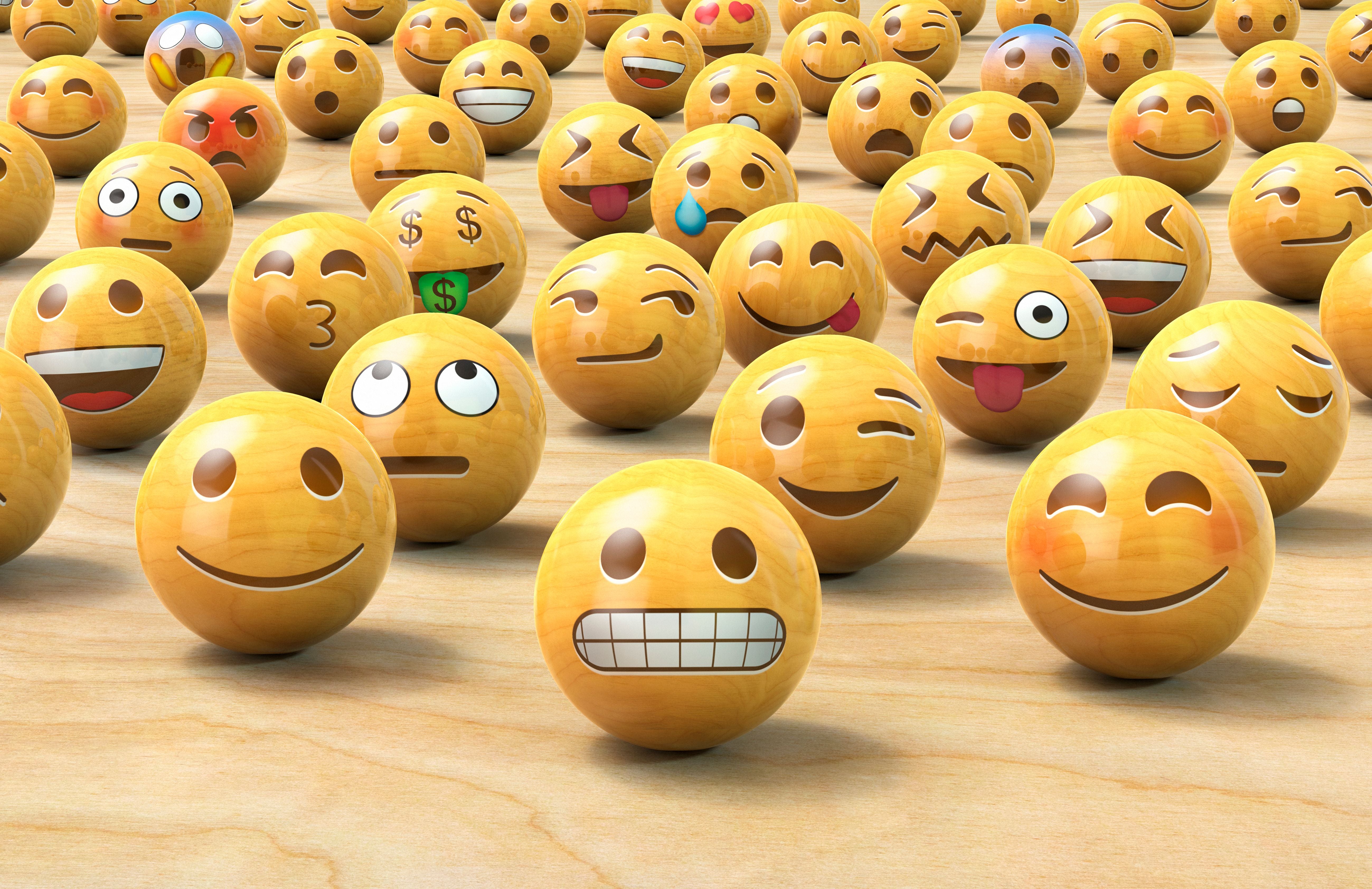 Viele Holzkugeln mit verschiedenen Emoji-Gesichtern stehen auf einer Holzfläche.