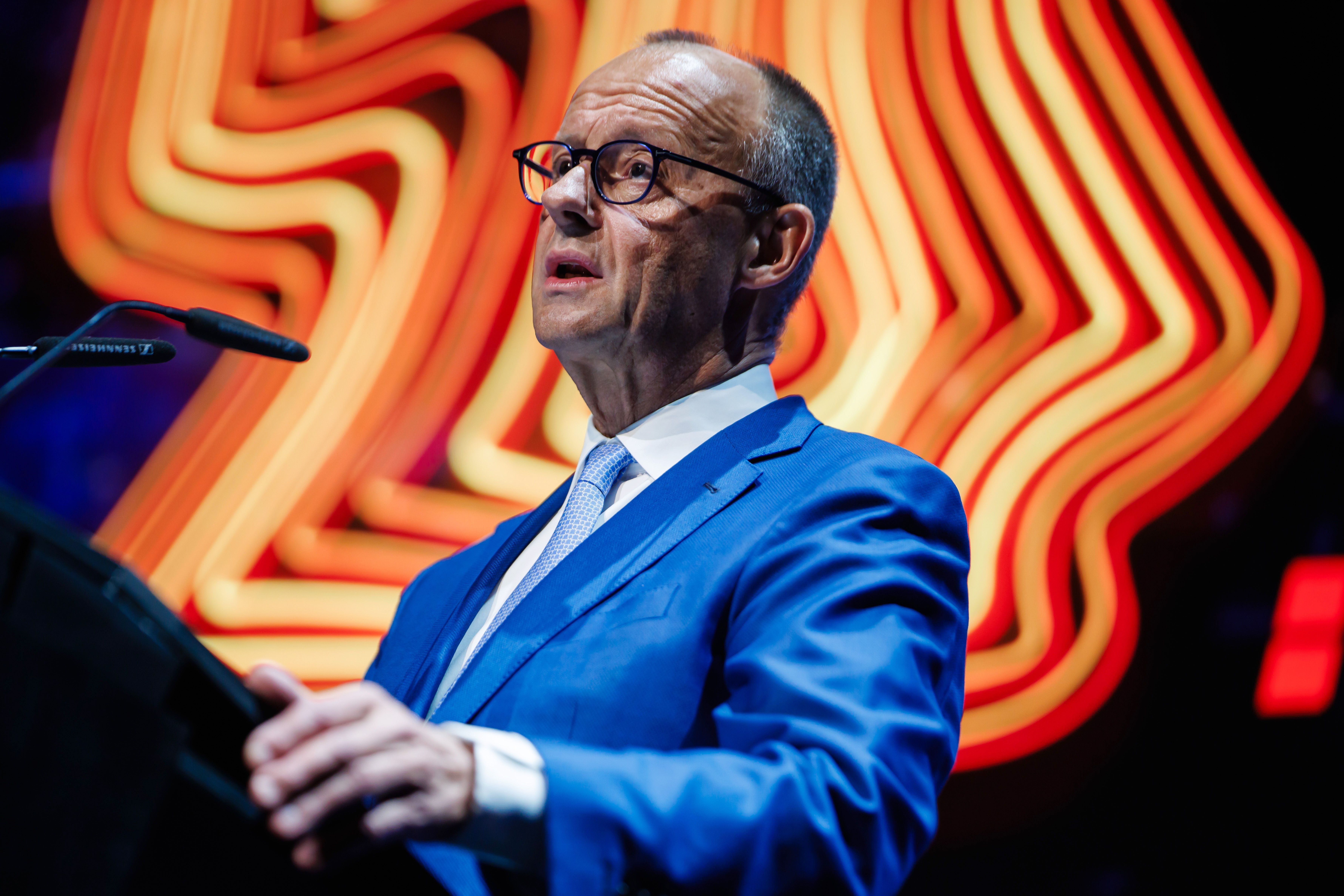 Ein Mann im blauen Anzug spricht bei einer Konferenz, im Hintergrund leuchtende Linien.