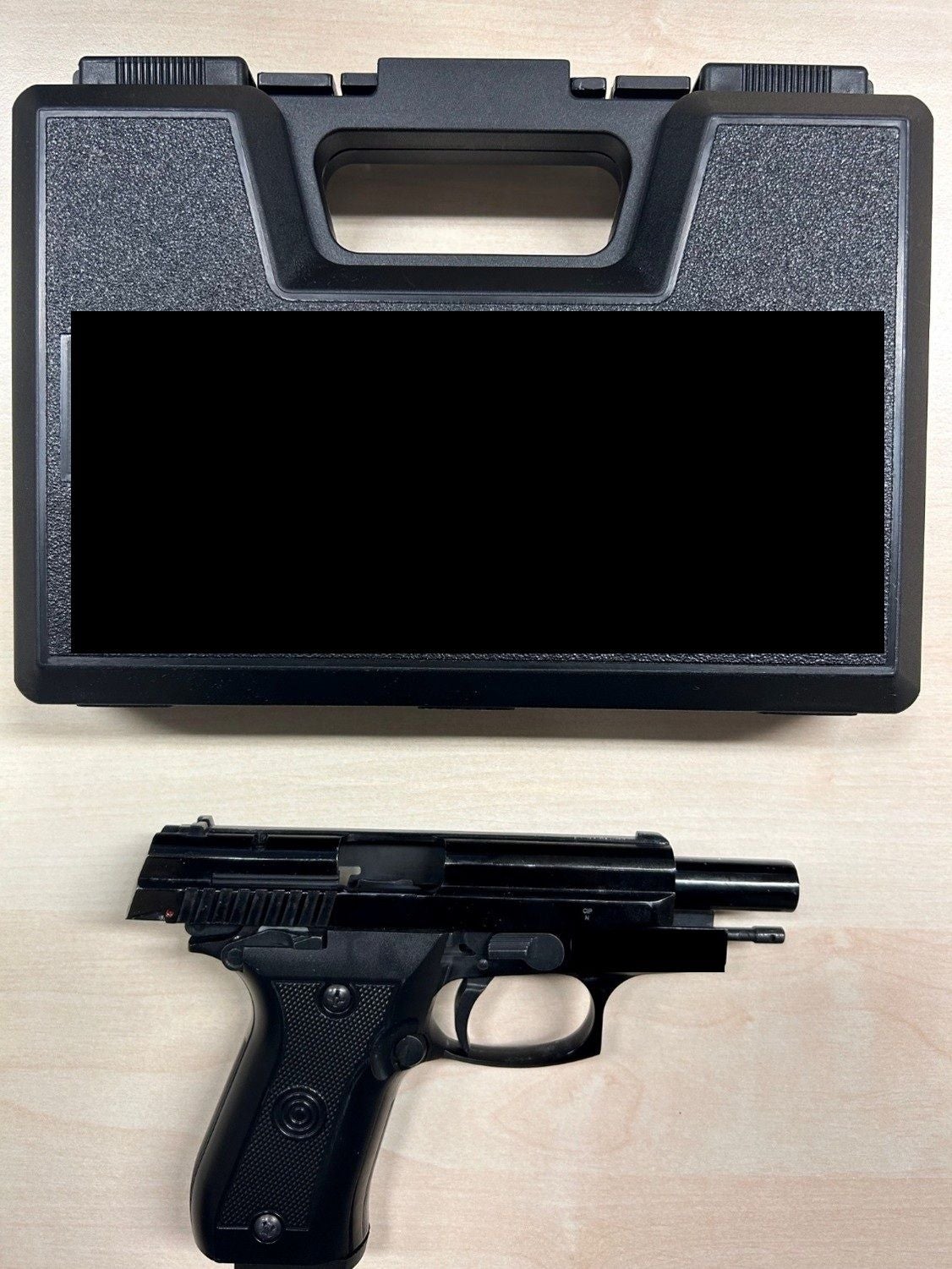 Eine schwarze Pistole liegt vor einem schwarzen Koffer auf einem hellen Tisch.