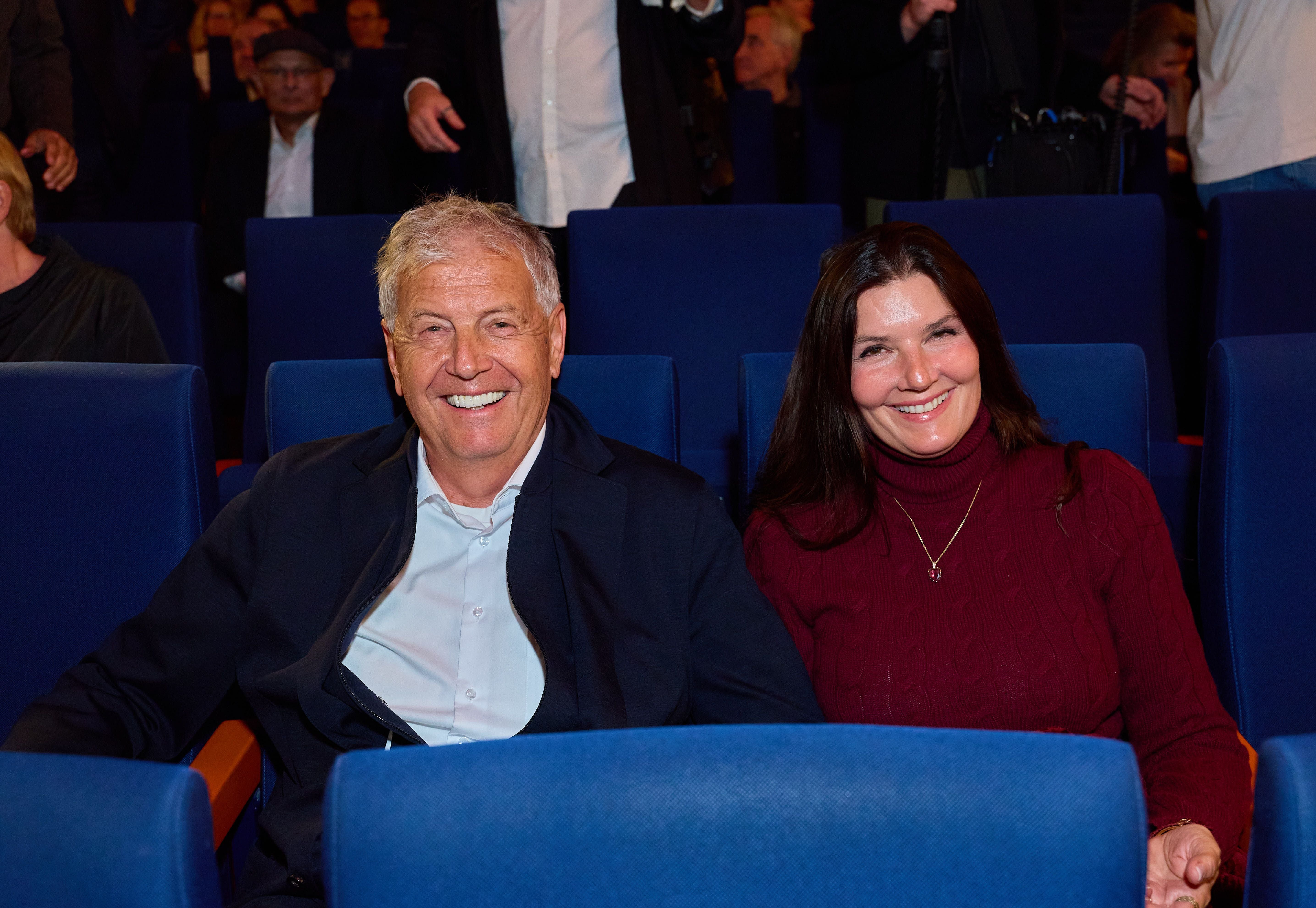 Ein lächelndes Paar sitzt in blauen Kinosesseln bei einer Filmpremiere.