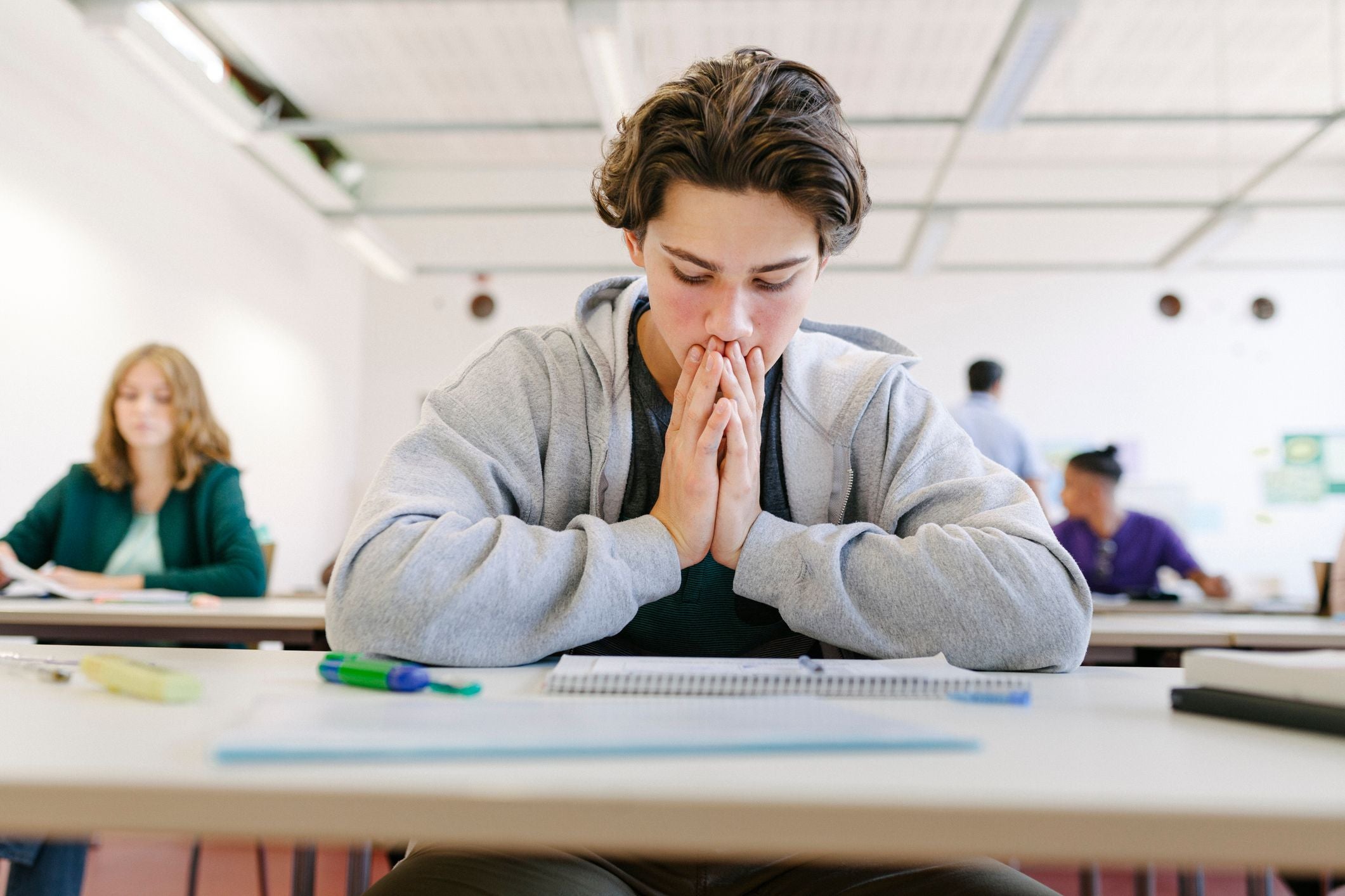 Schüler sitzt nachdenklich vor einem Testblatt im Klassenraum während einer Prüfung.
