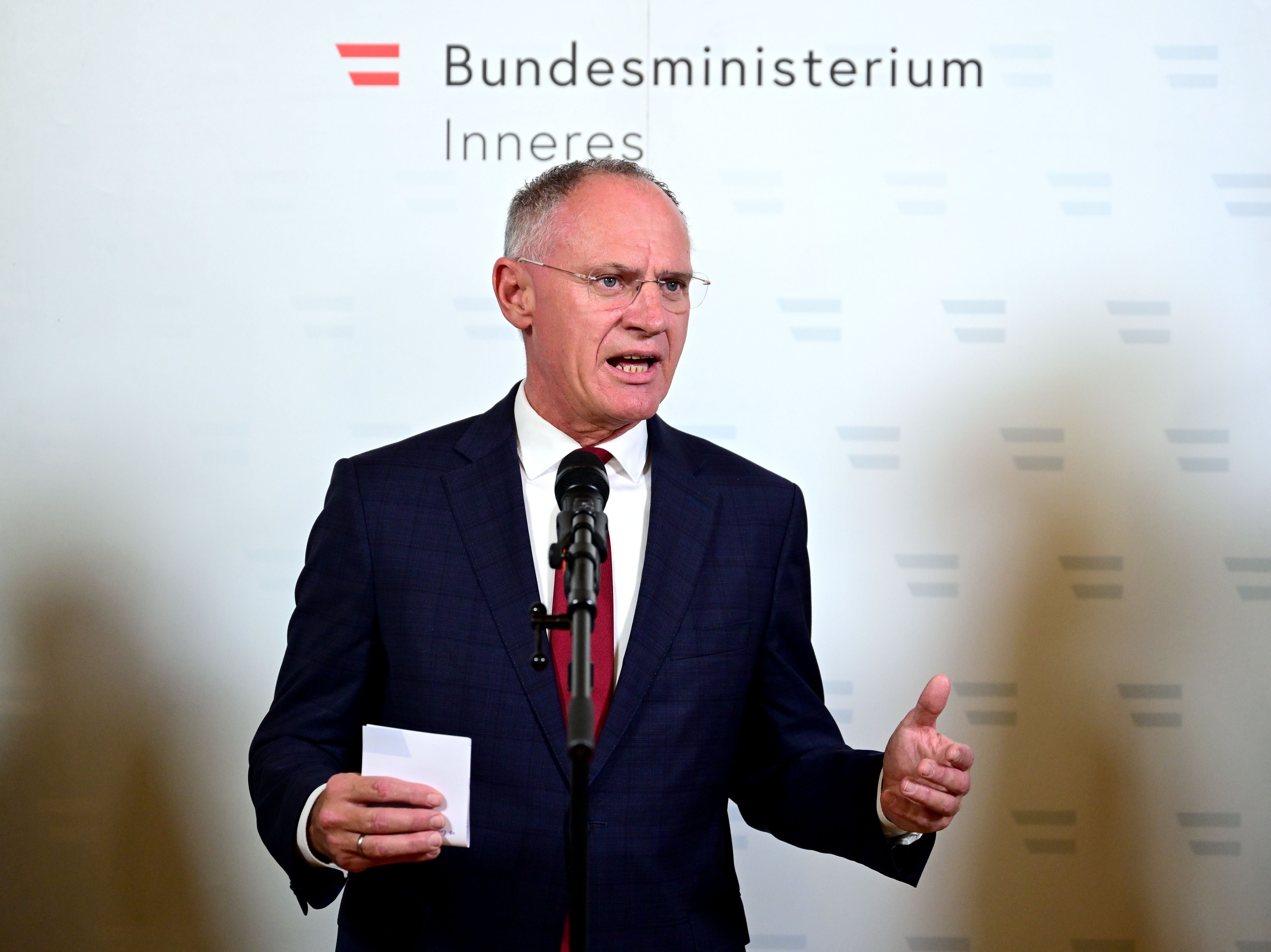 Ein Mann im Anzug spricht bei einer Pressekonferenz vor dem Logo des Innenministeriums.