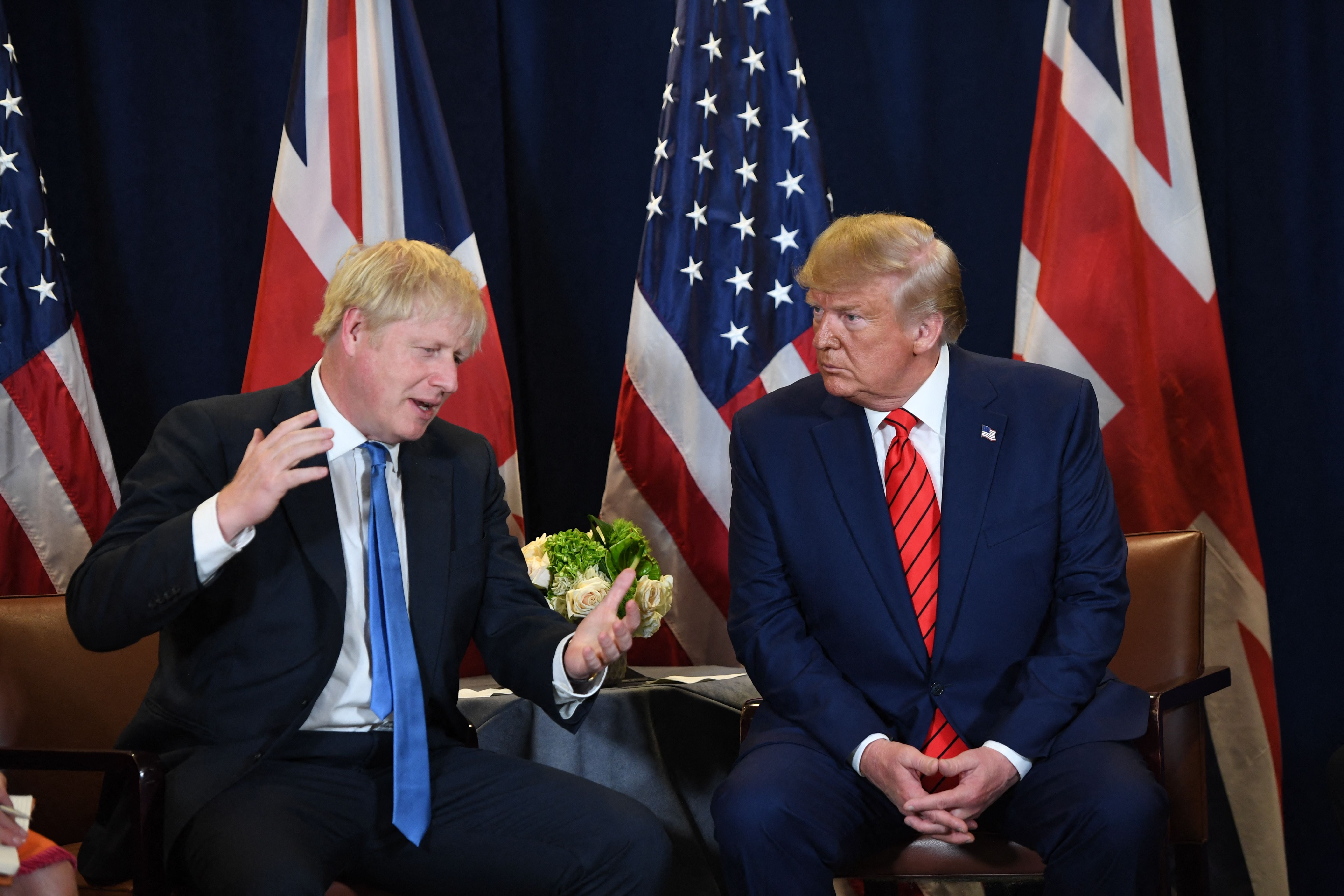 Zwei Männer im Anzug sitzen vor US- und UK-Flaggen und unterhalten sich angeregt.