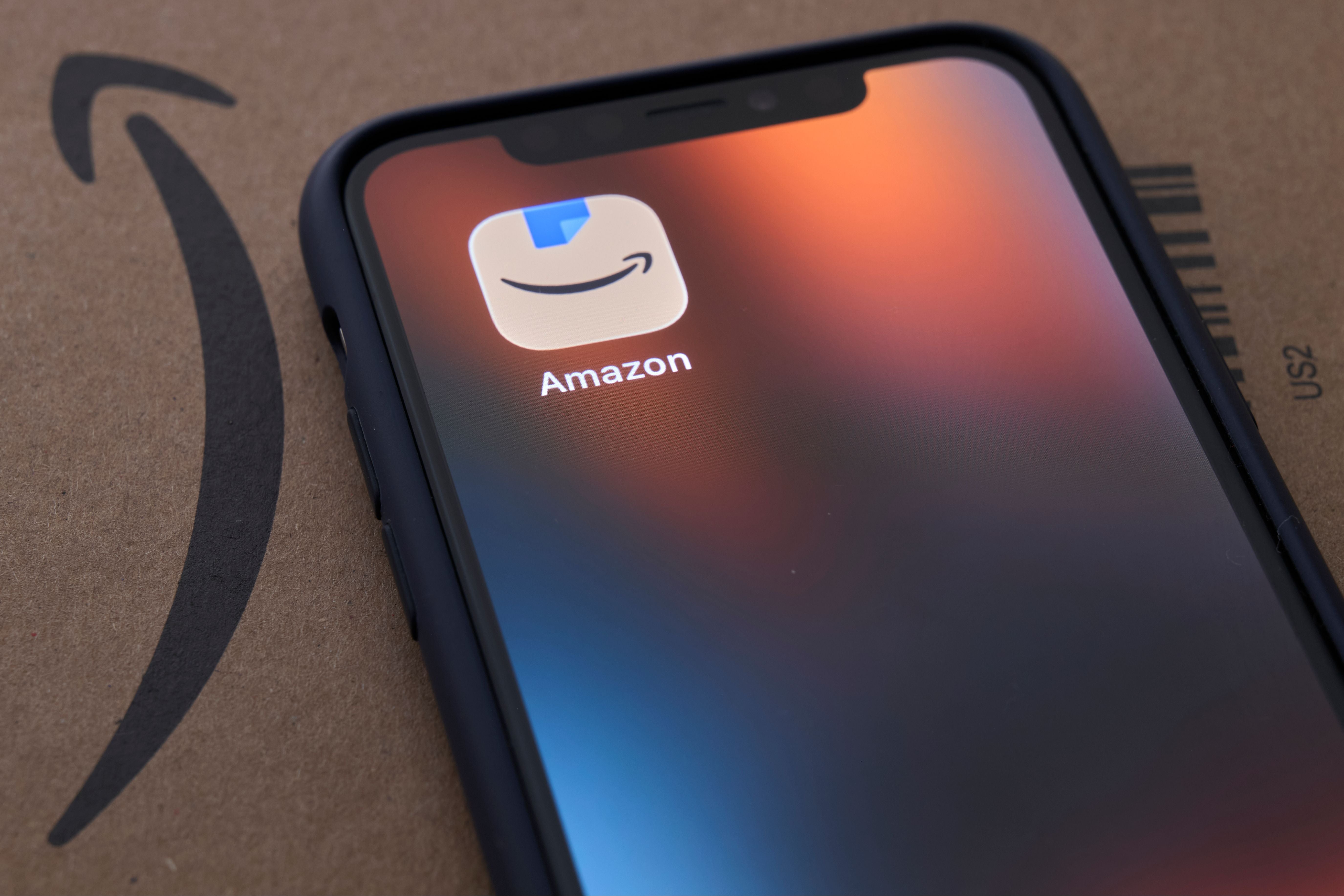 Smartphone mit Amazon-App liegt auf einem Amazon-Paket mit Smile-Logo und Barcode.