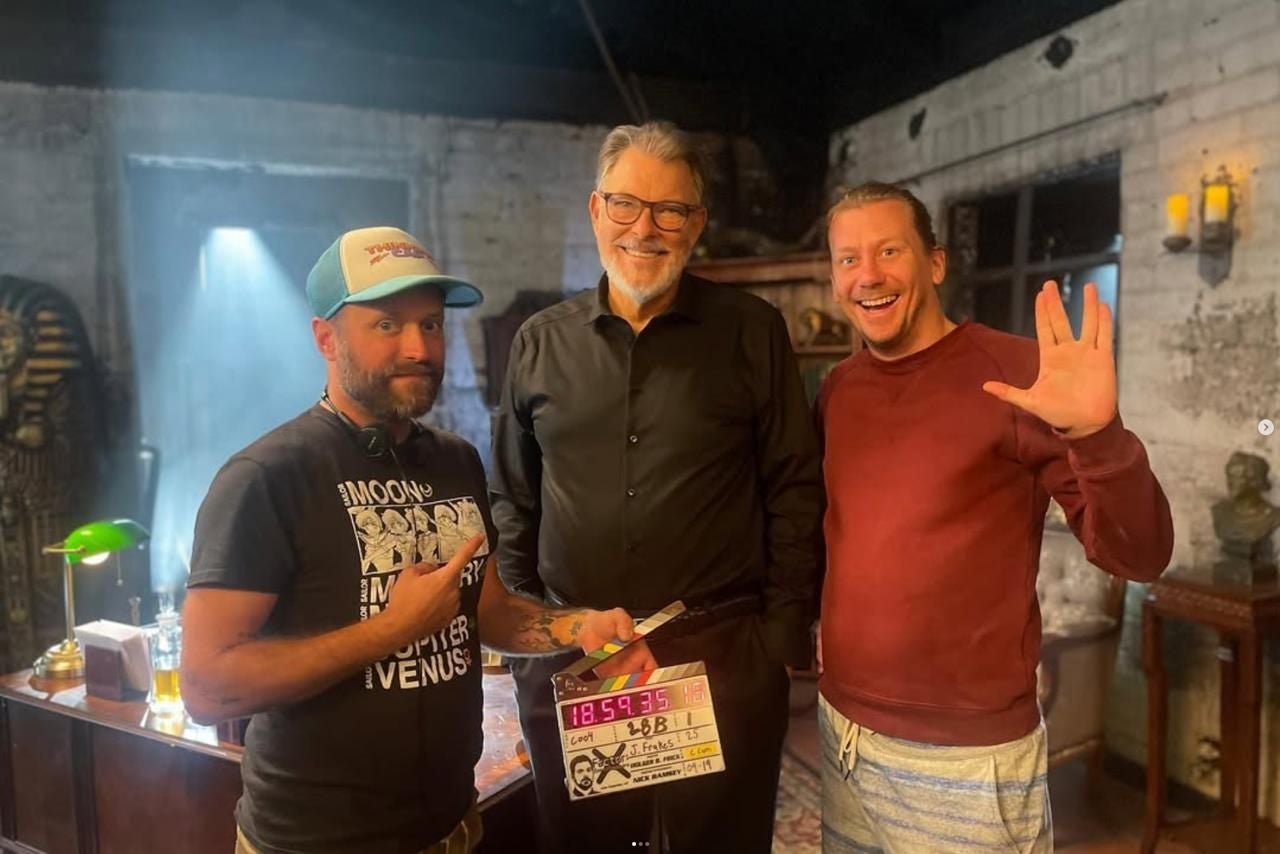 Drei Männer stehen lächelnd am Filmset, einer hält eine Filmklappe, einer zeigt den Vulkaniergruß.