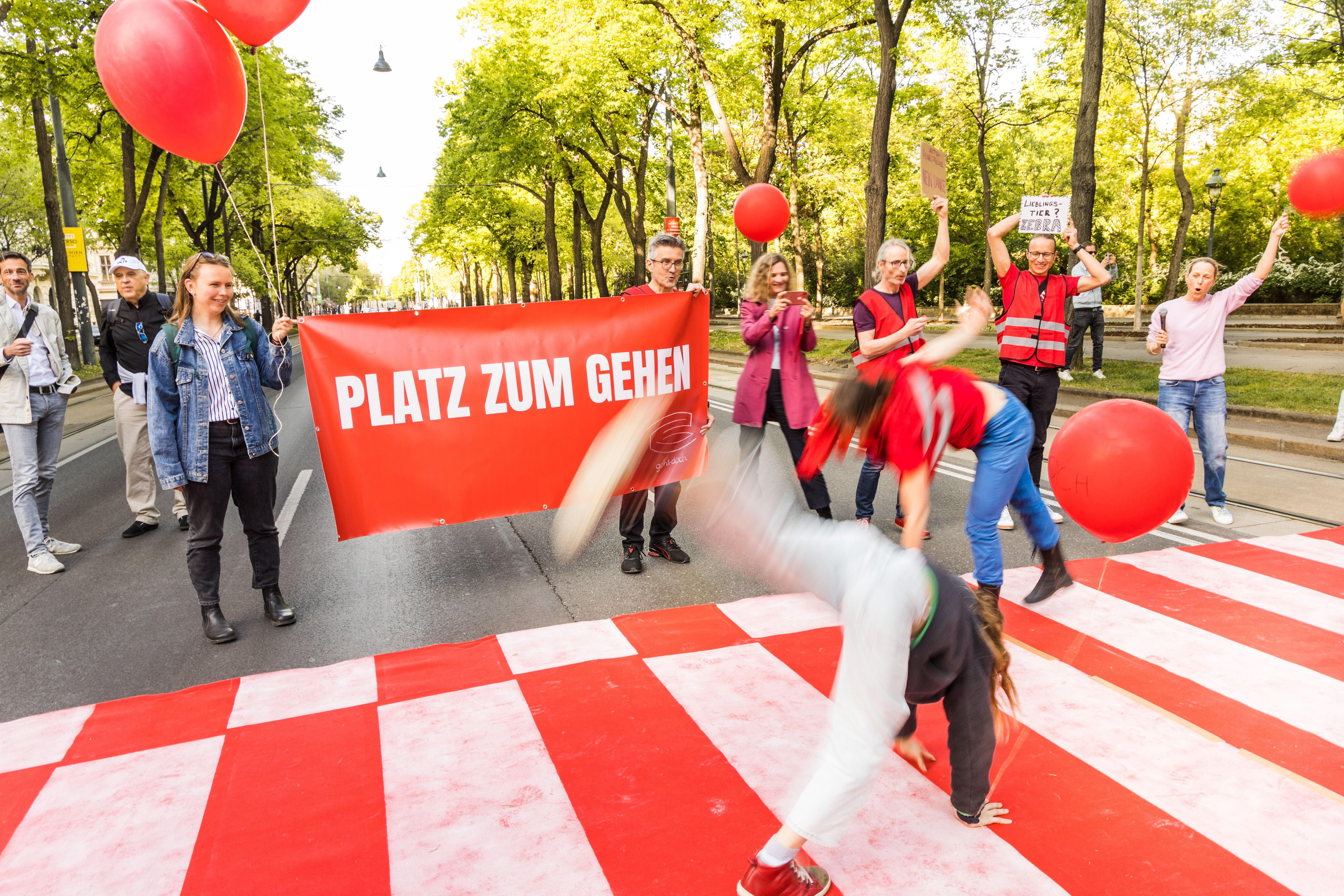 Menschen mit roten Ballons und Banner „Platz zum Gehen“ protestieren auf einer Straße.