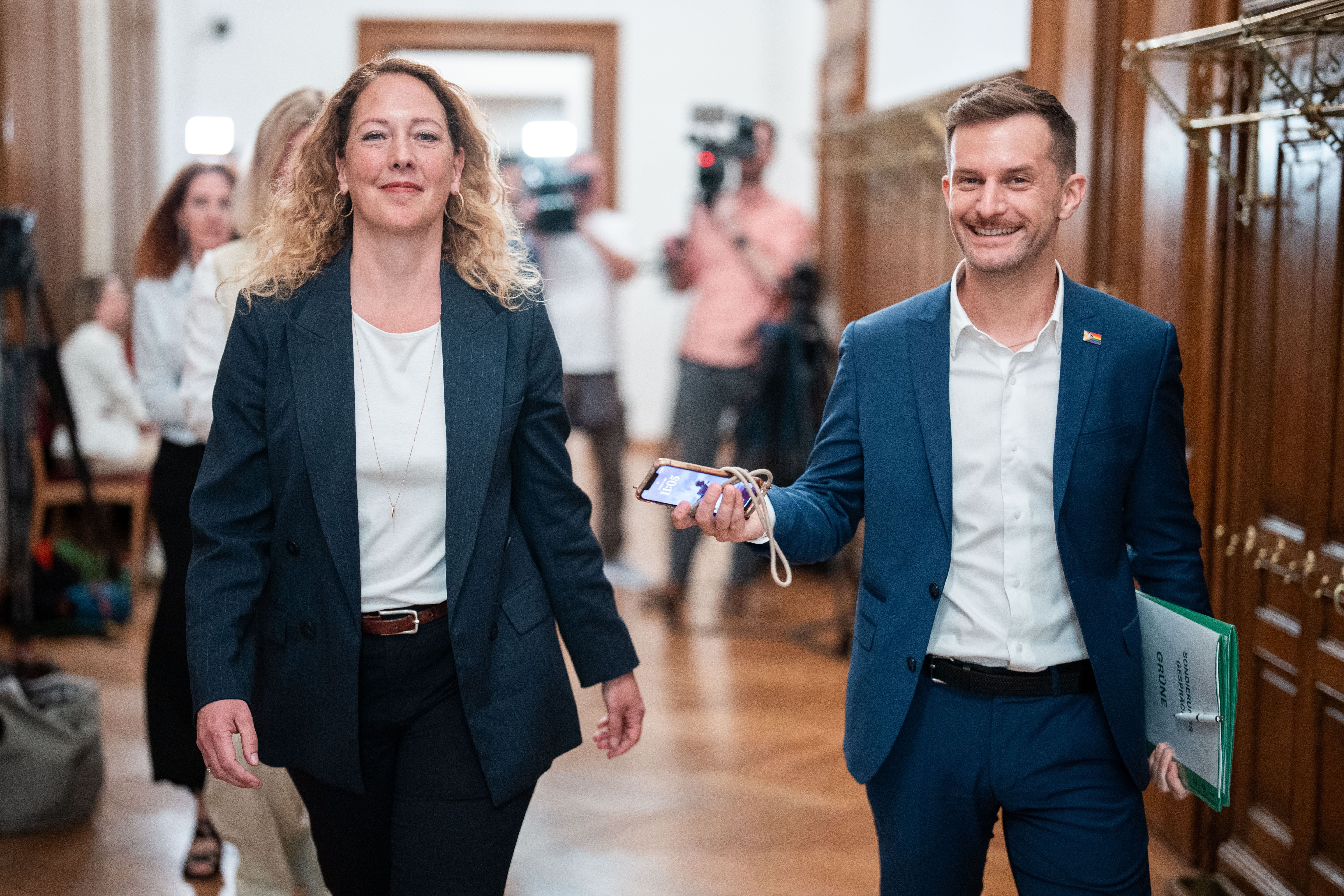 Zwei Personen im Anzug gehen lächelnd durch einen Flur nach Koalitionsgesprächen.