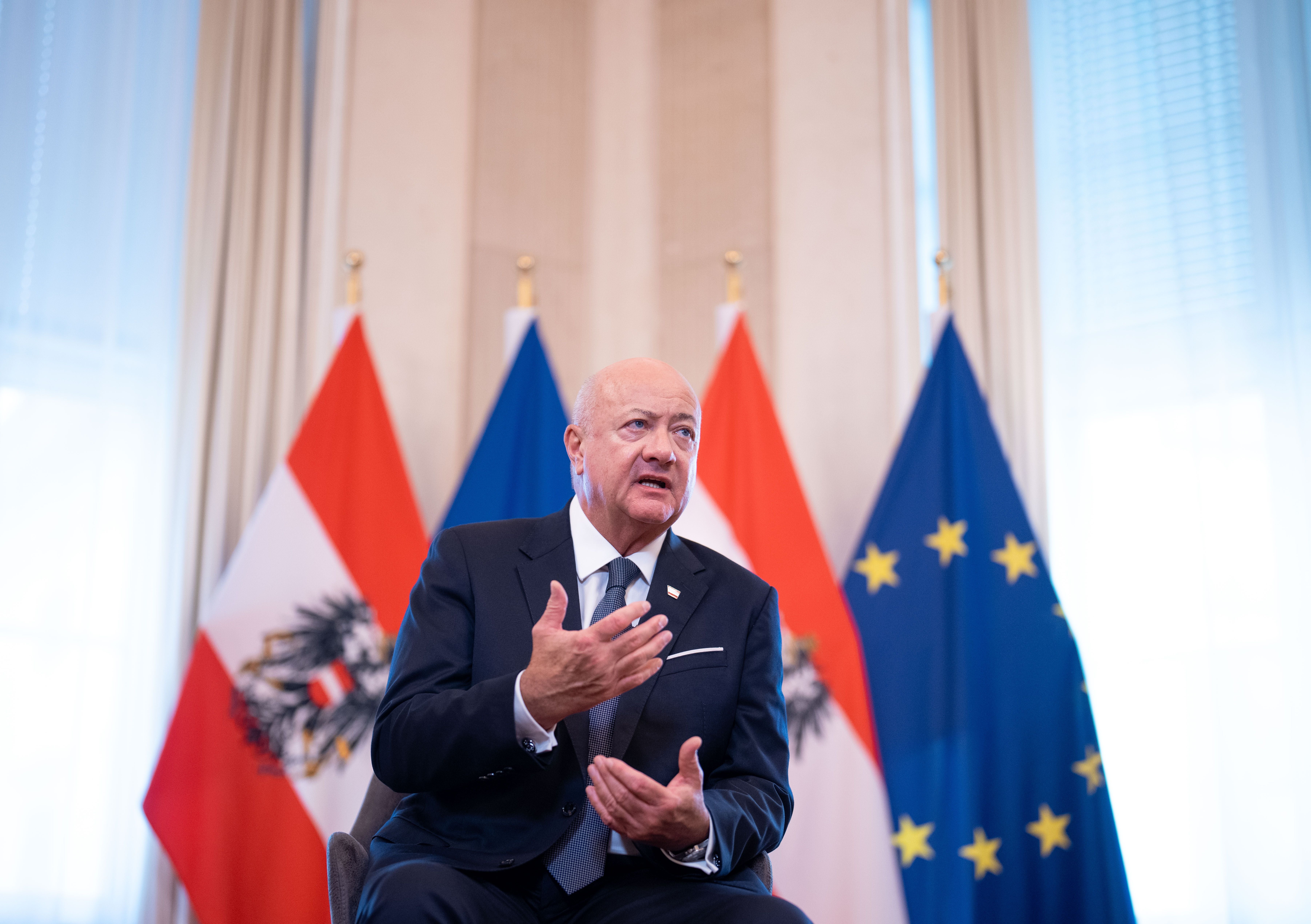 Ein Mann im Anzug spricht vor österreichischen und EU-Flaggen bei einem Interview.