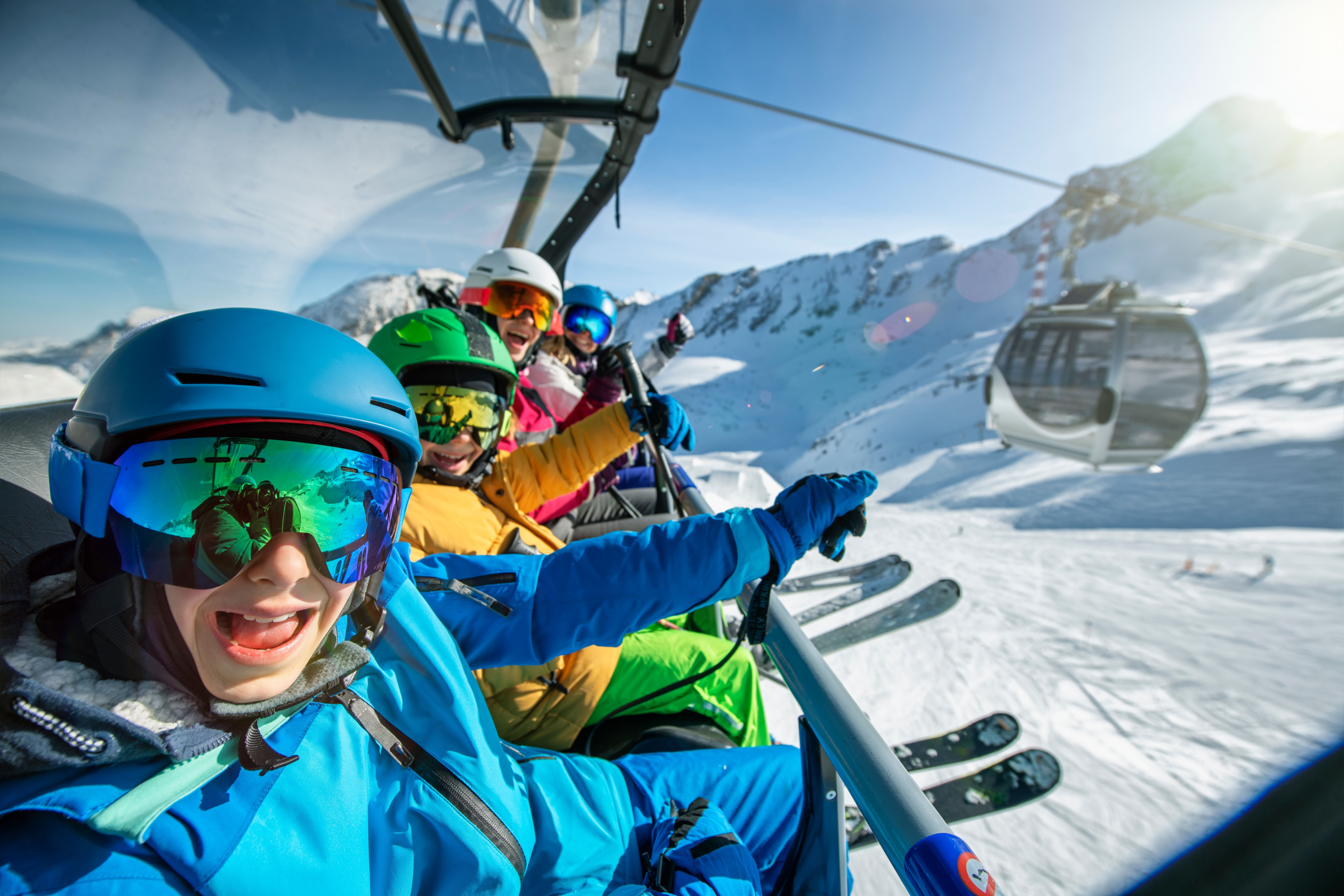 Familie mit Skiausrüstung fährt lachend im Sessellift durch verschneite Alpenlandschaft.