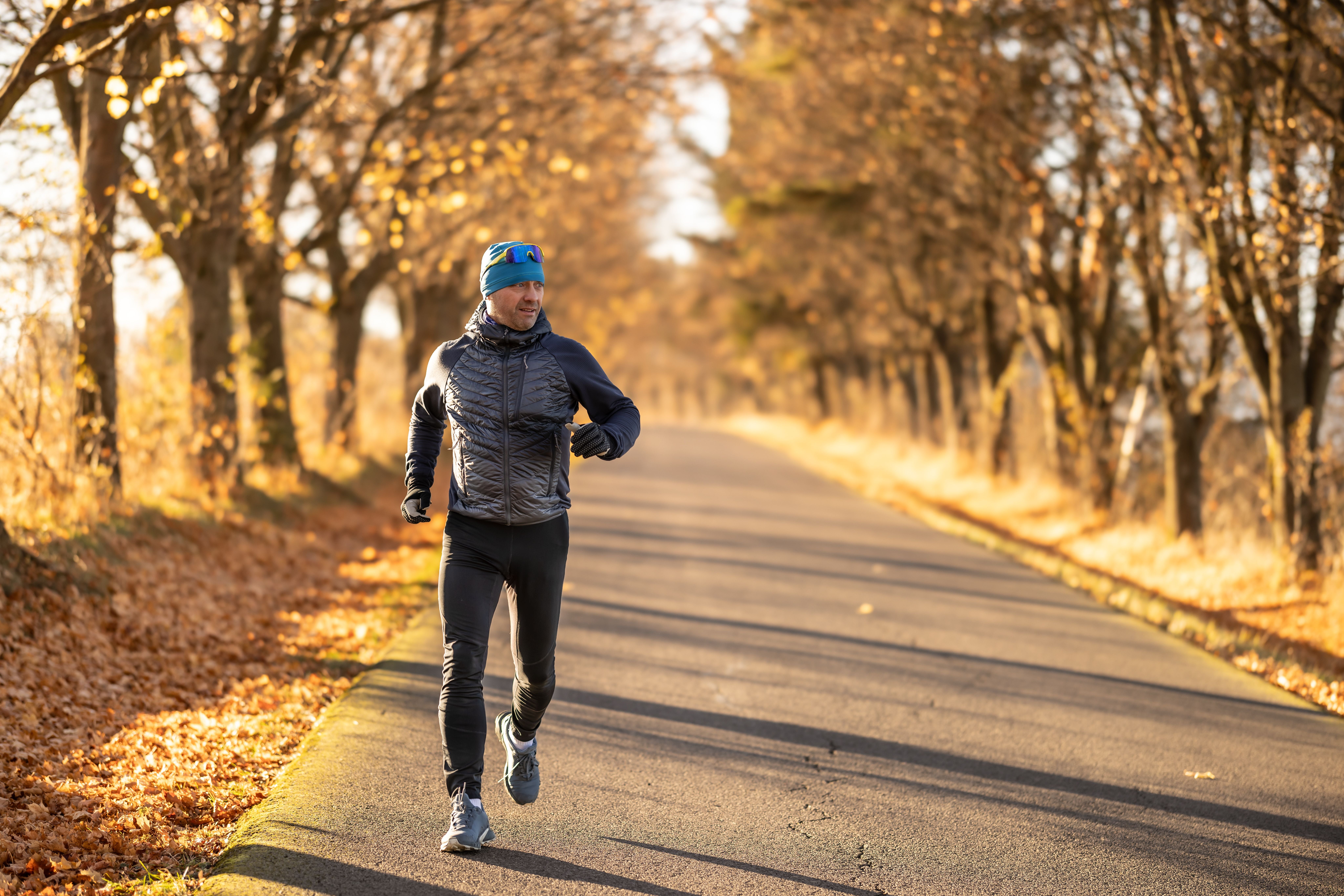 Mann joggt auf herbstlicher Straße, umgeben von Bäumen mit goldenem Laub, sonniges Wetter.