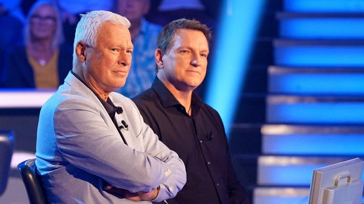 Zwei Männer sitzen nebeneinander in einem Fernsehstudio mit blauem Hintergrund.