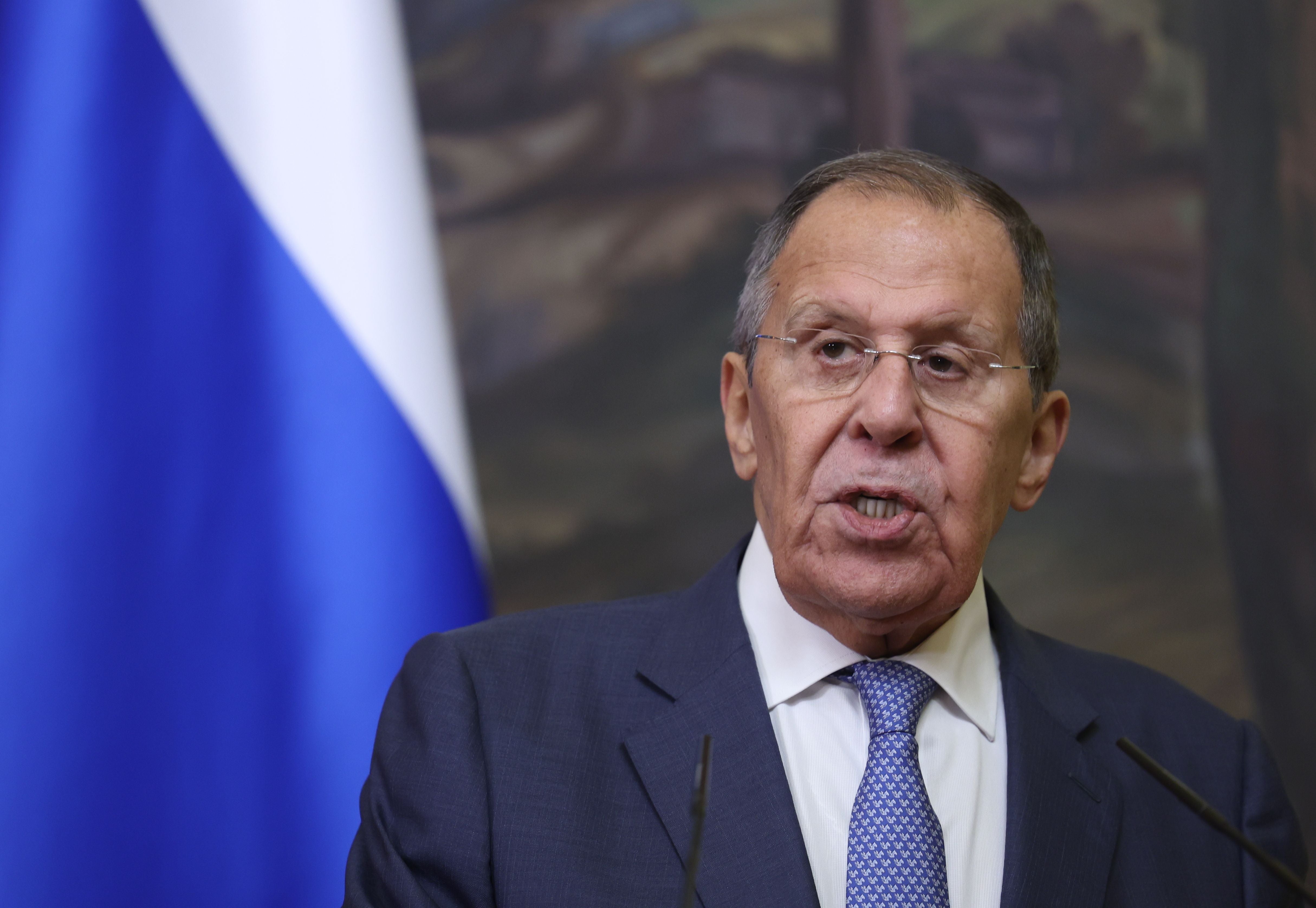 Ein Mann im Anzug spricht bei einer Pressekonferenz vor einer russischen Flagge.