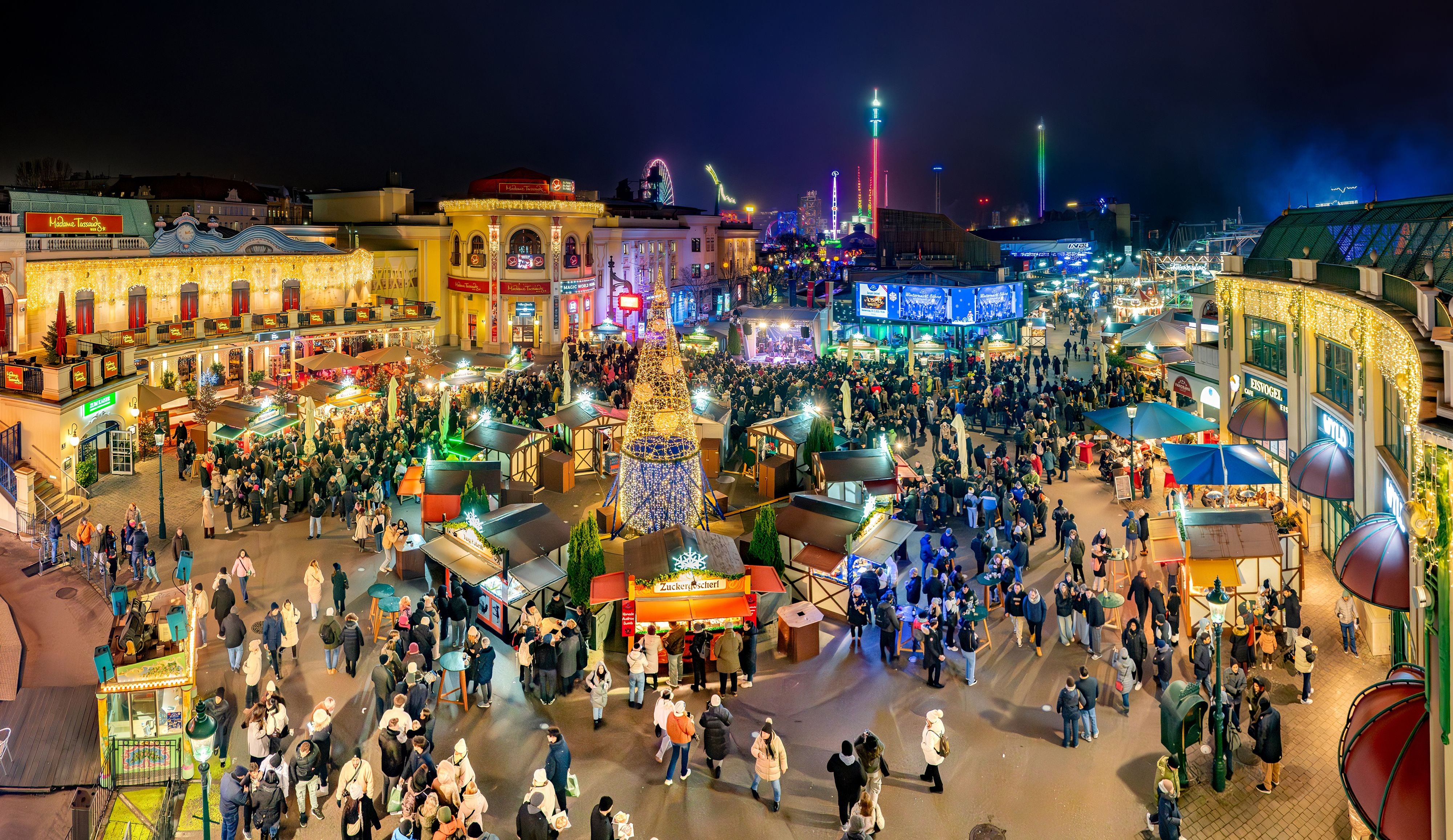 Großer, festlich beleuchteter Weihnachtsmarkt im Prater mit vielen Besuchern und Buden bei Nacht.