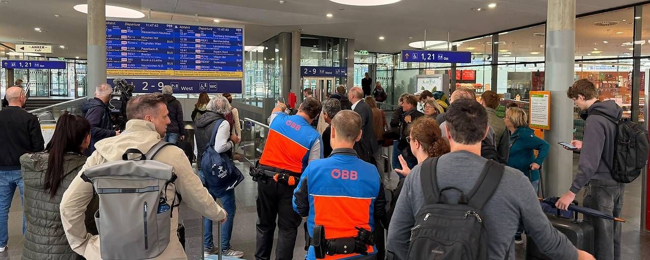 Menschen versammeln sich am Bahnhof vor einer Anzeigetafel, ÖBB-Personal ist sichtbar.