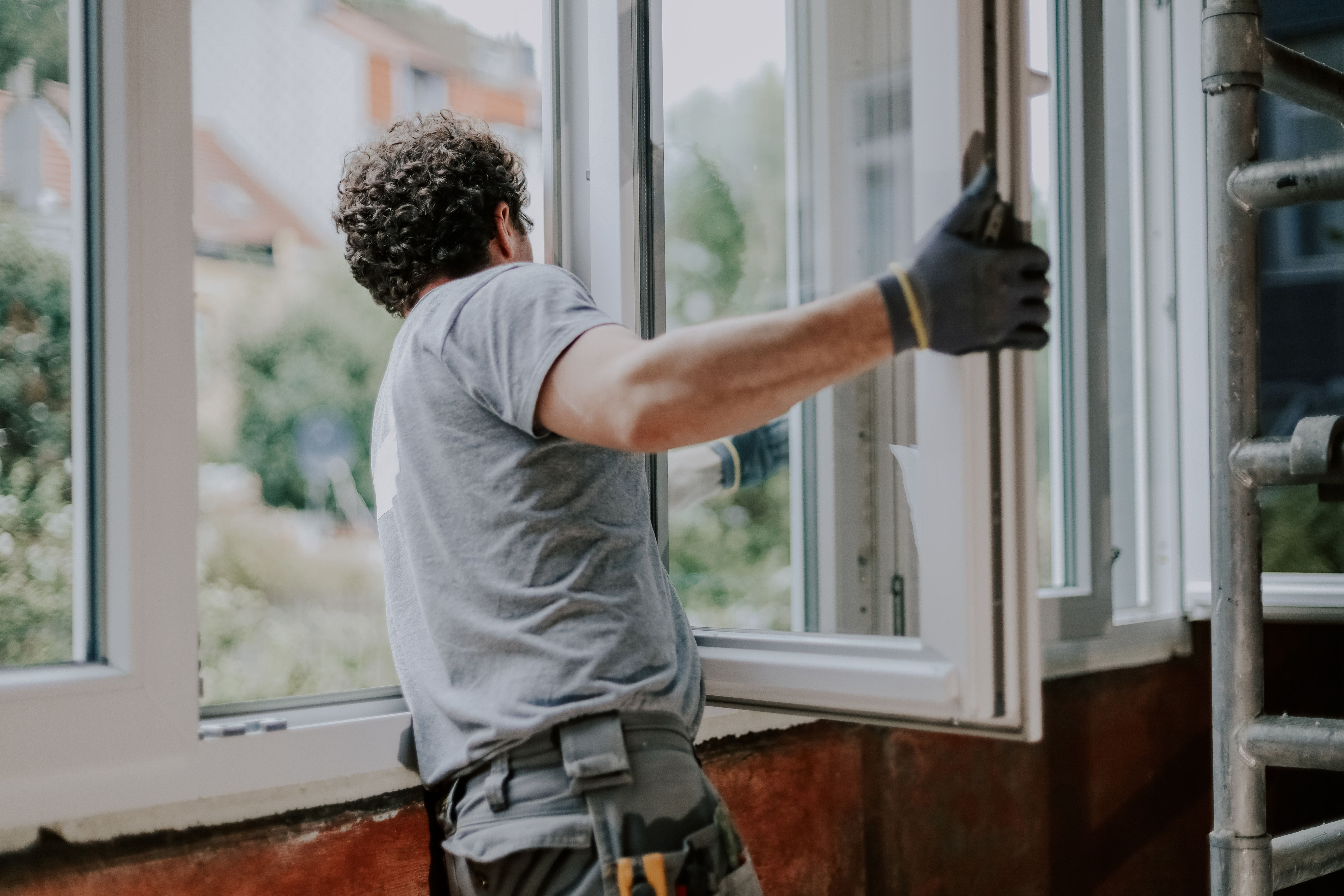 Ein Mann installiert von innen ein Fensterrahmen in einem Haus bei Tageslicht.
