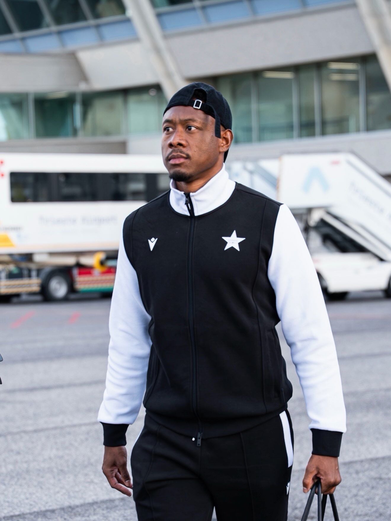 Ein Mann in schwarzem Trainingsanzug und Basecap läuft auf einem Flughafen entlang.