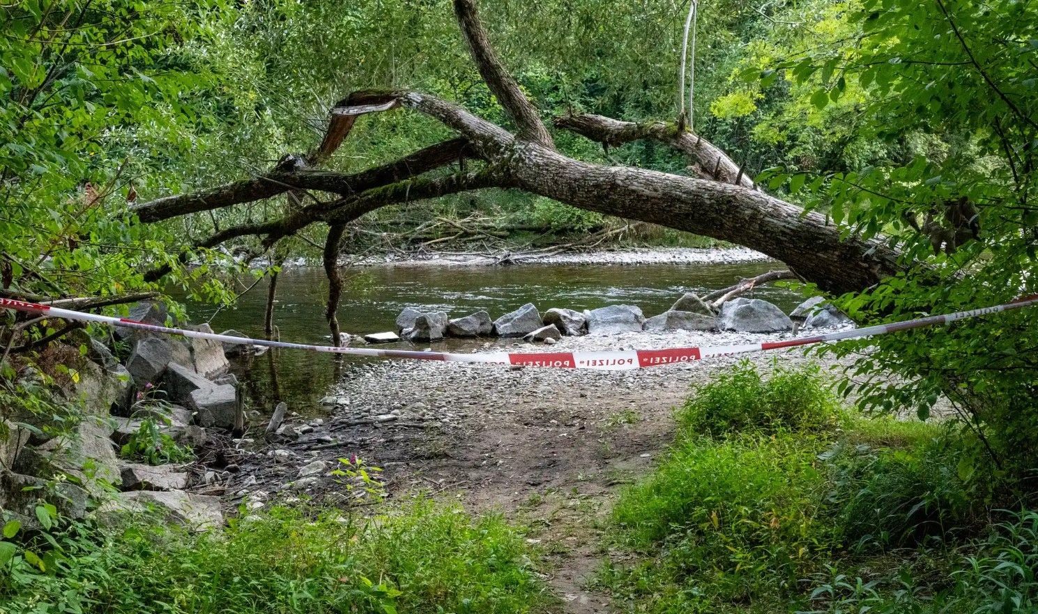 Ein Flussufer im Wald ist mit Polizeiabsperrband abgesperrt.