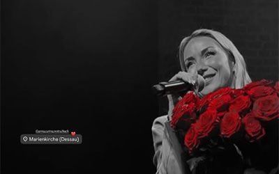 Anna-Carina Woitschack mit Mikrofon hält einen Strauß roter Rosen, Hintergrund in Schwarzweiß.