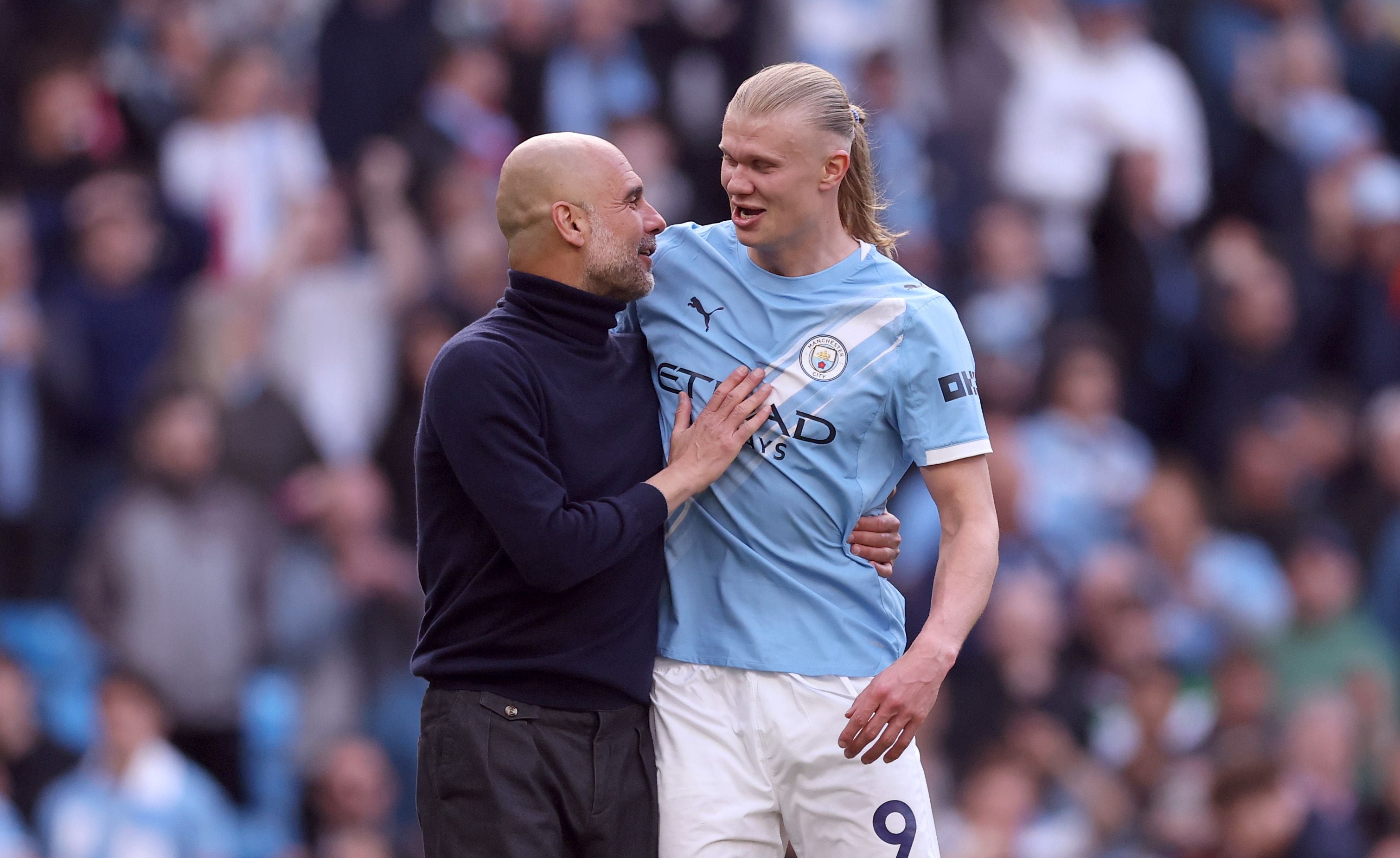 Erling Haaland und Pep Guardiola von Manchester City stehen eng umschlungen auf dem Spielfeld und unterhalten sich lächelnd.