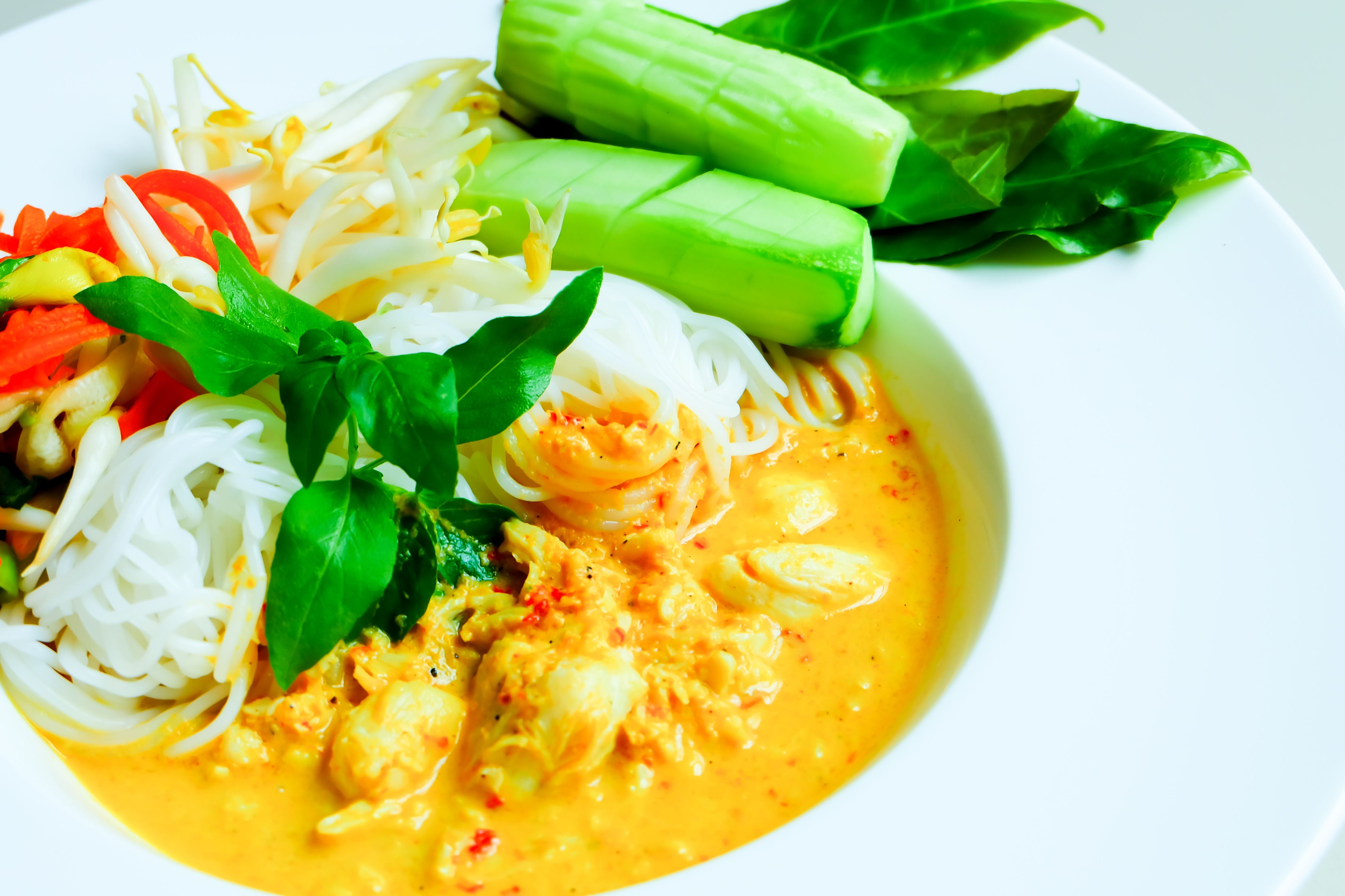 Reisnudeln in Fischcurrysauce mit Gemüse und frischen Kräutern auf einem weißen Teller.