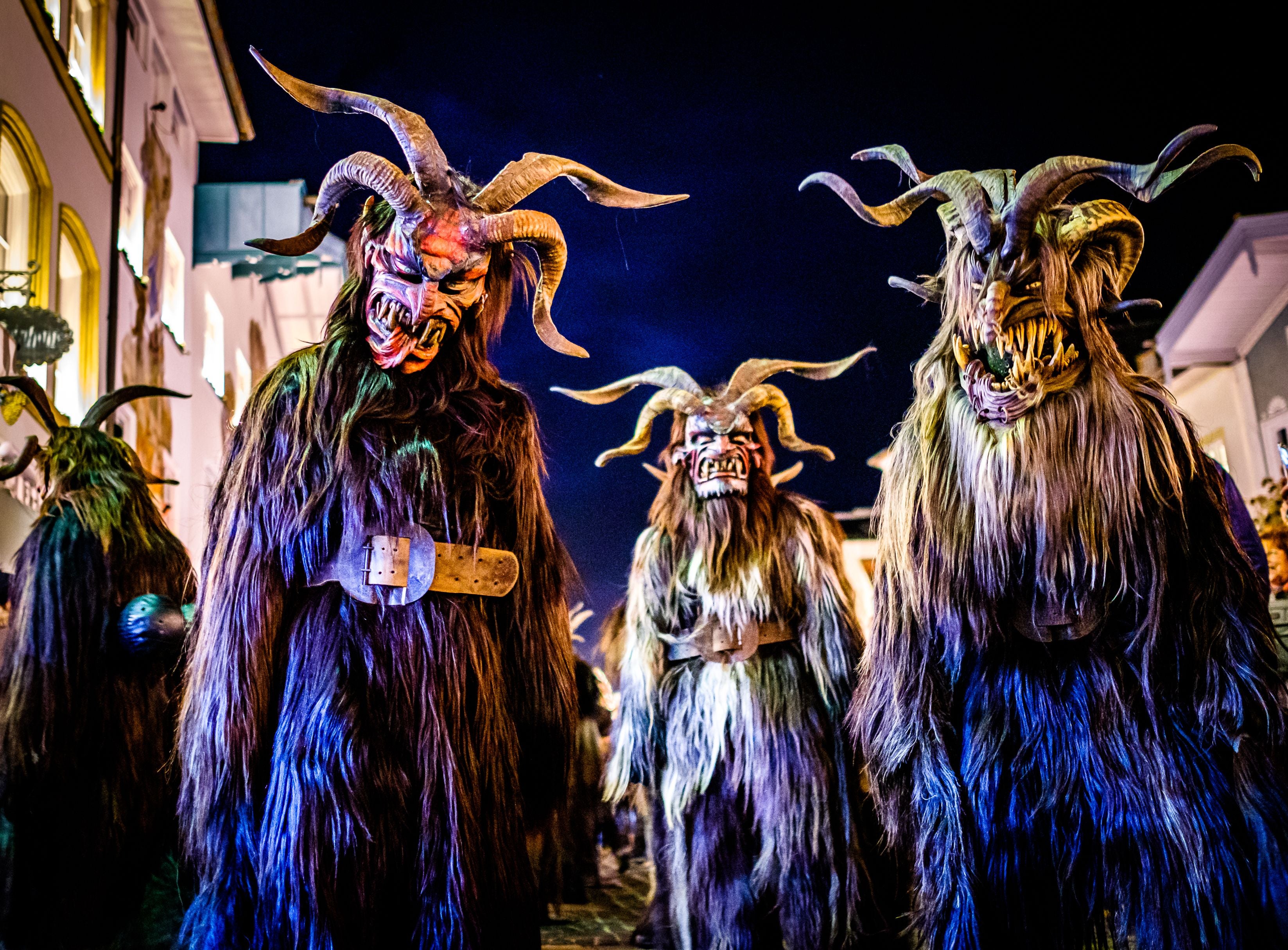 Drei als Krampus verkleidete Personen mit zotteligen Fellkostümen und dämonischen Masken bei Nacht.