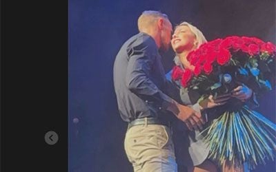 Eine Frau hält einen großen Strauß roter Rosen und lächelt, während ein Mann sie umarmt.