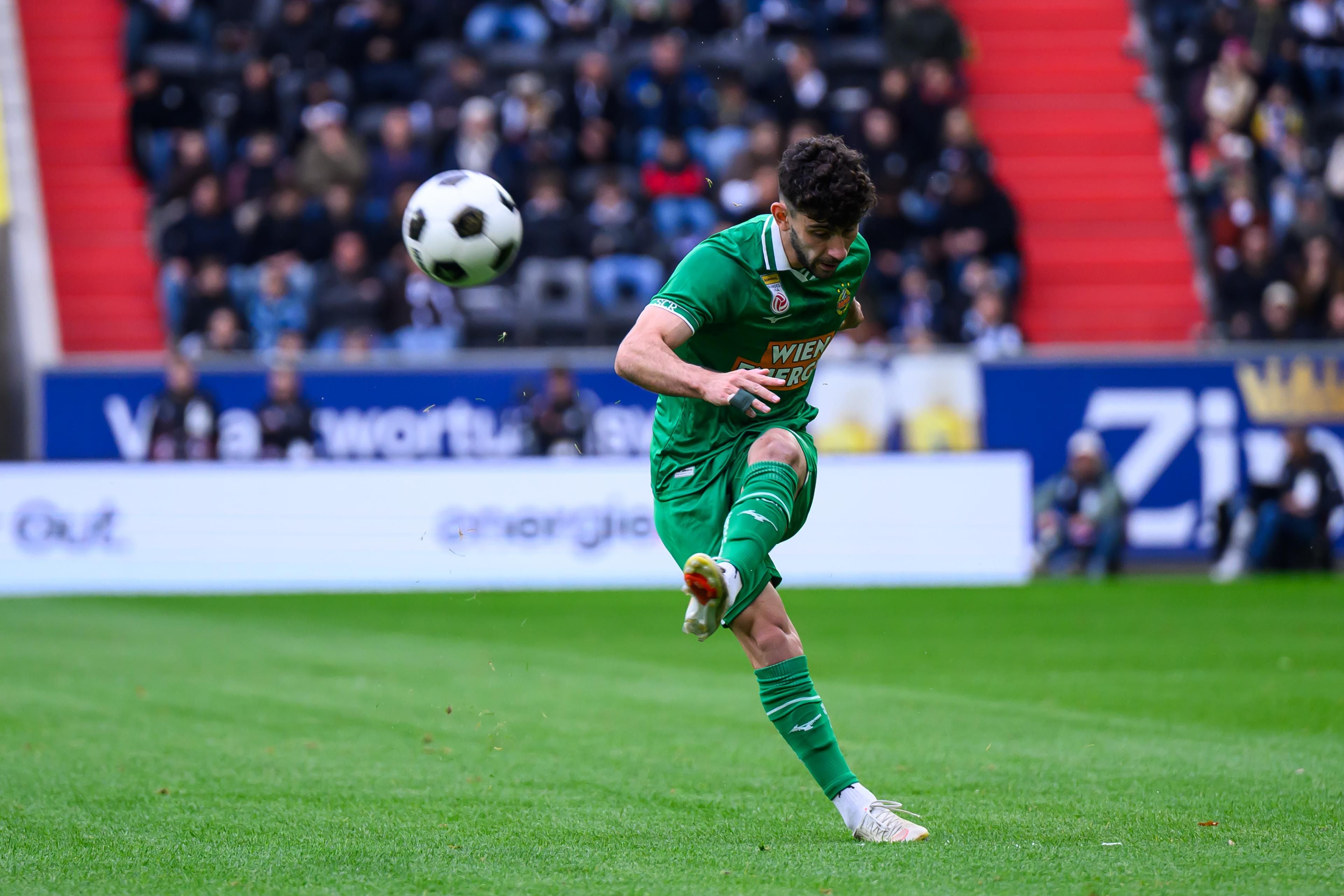 Ein Fußballspieler im grünen Trikot schießt den Ball auf einem Stadionfeld.