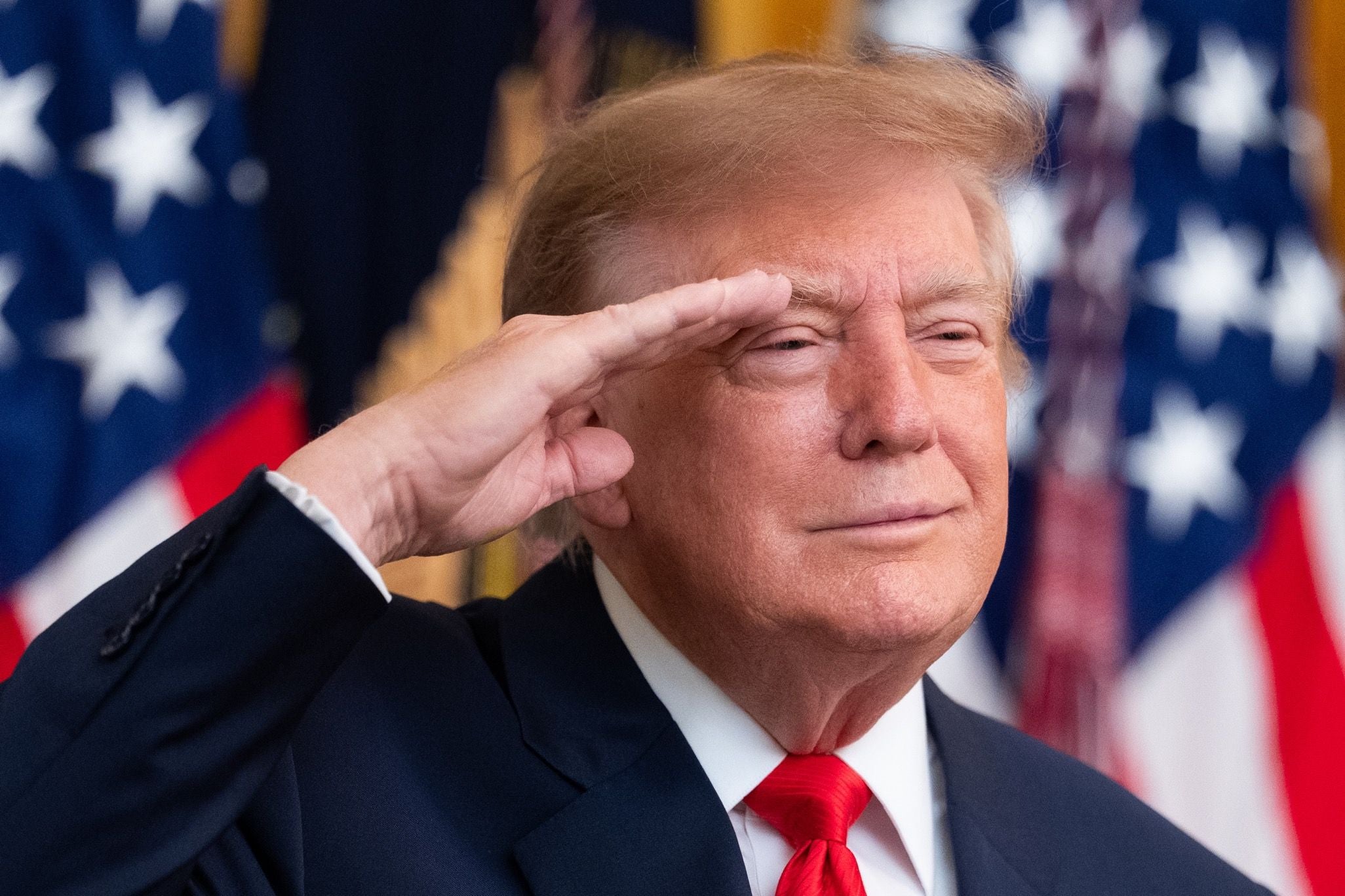 Ein Mann im Anzug salutiert vor US-Flaggen im Hintergrund.