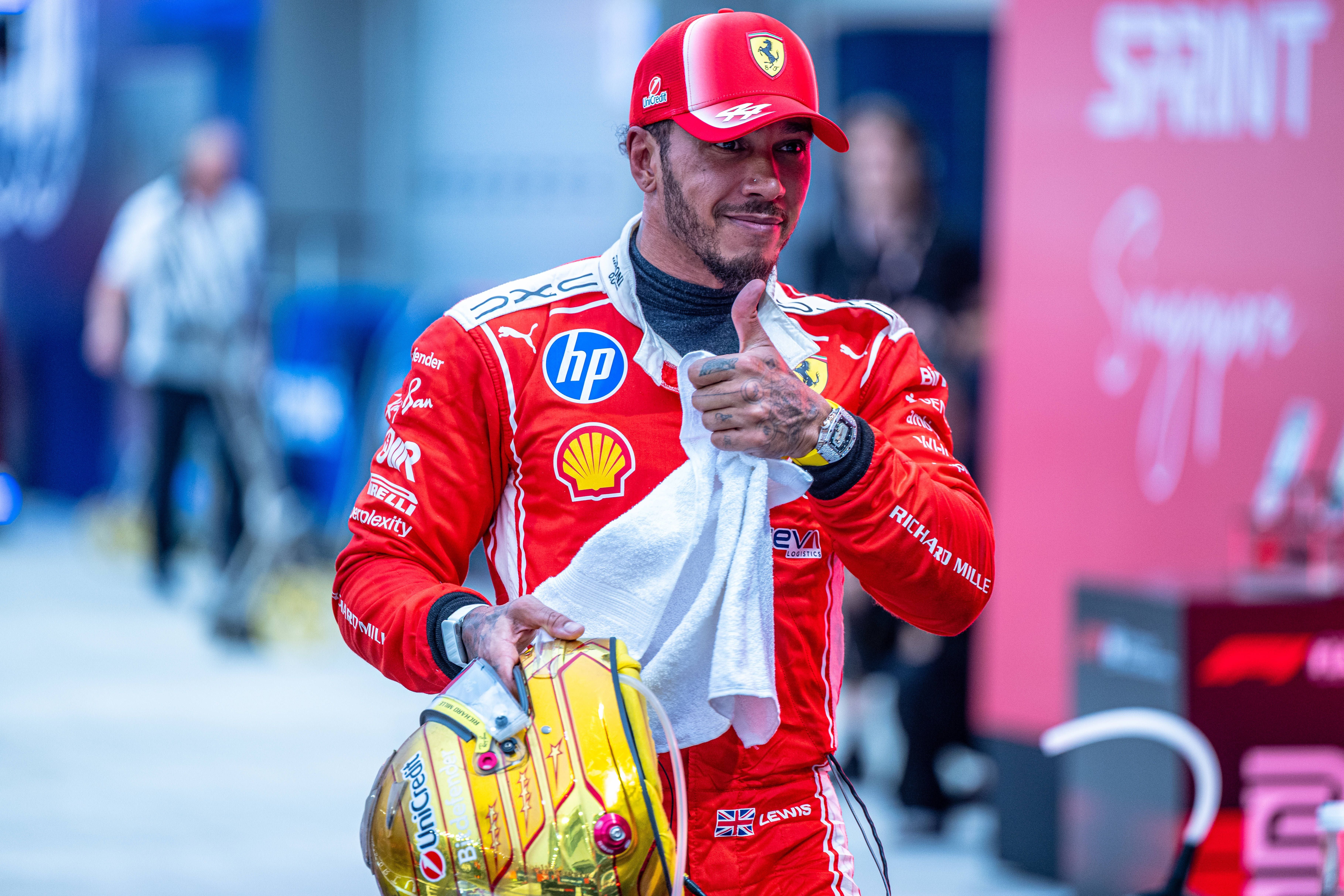 Ein Formel-1-Fahrer im roten Ferrari-Anzug hält einen Helm und ein Handtuch in der Boxengasse.