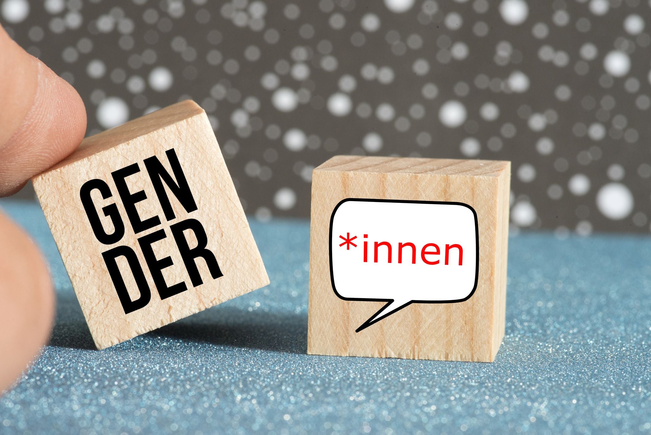 Zwei Holzwürfel mit den Aufschriften "GENDER" und "*innen" in einer Sprechblase.