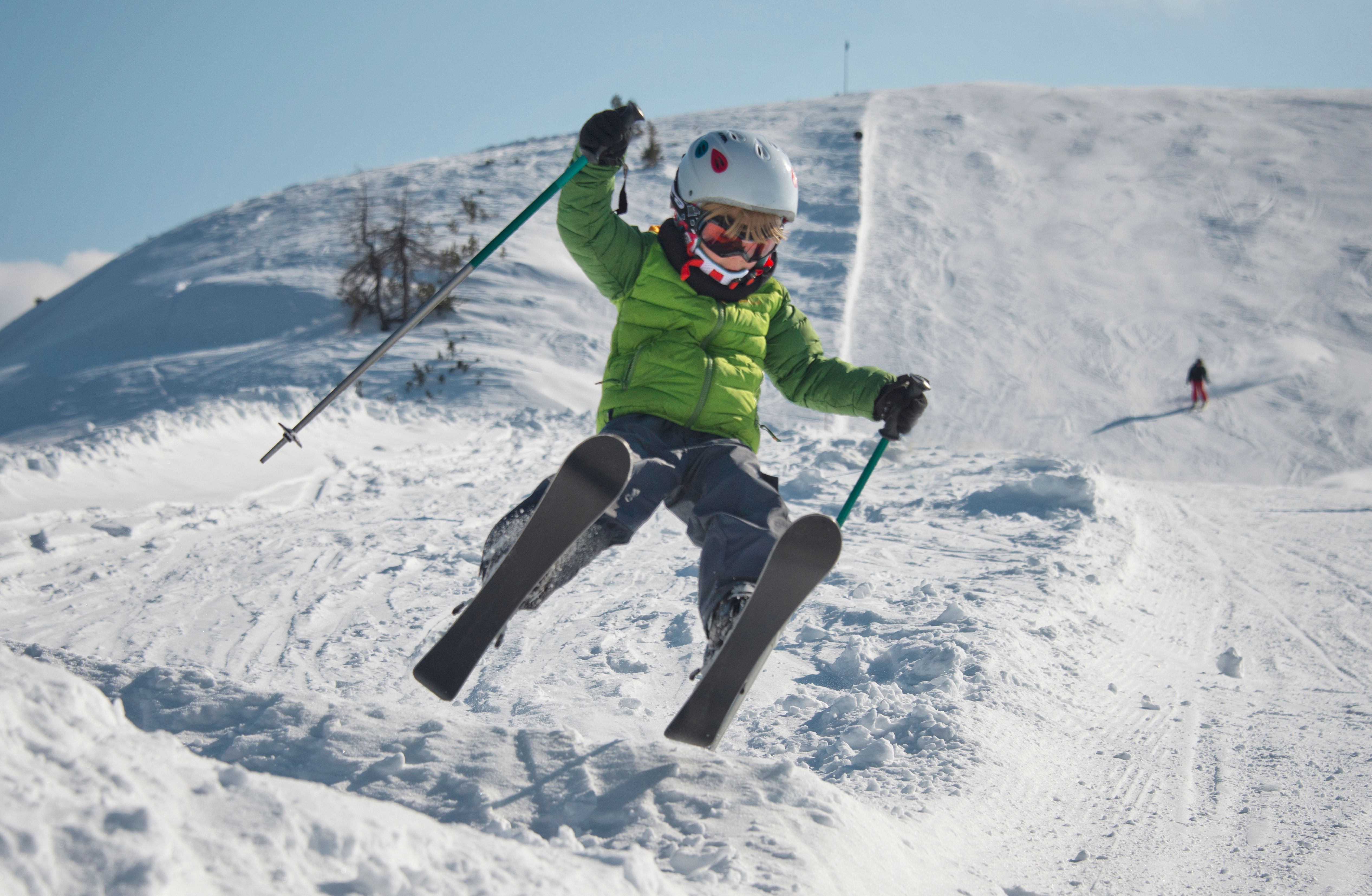 Kind springt mit Skiern über eine kleine Schneerampe auf einer Skipiste in Zauchensee, Salzburg.