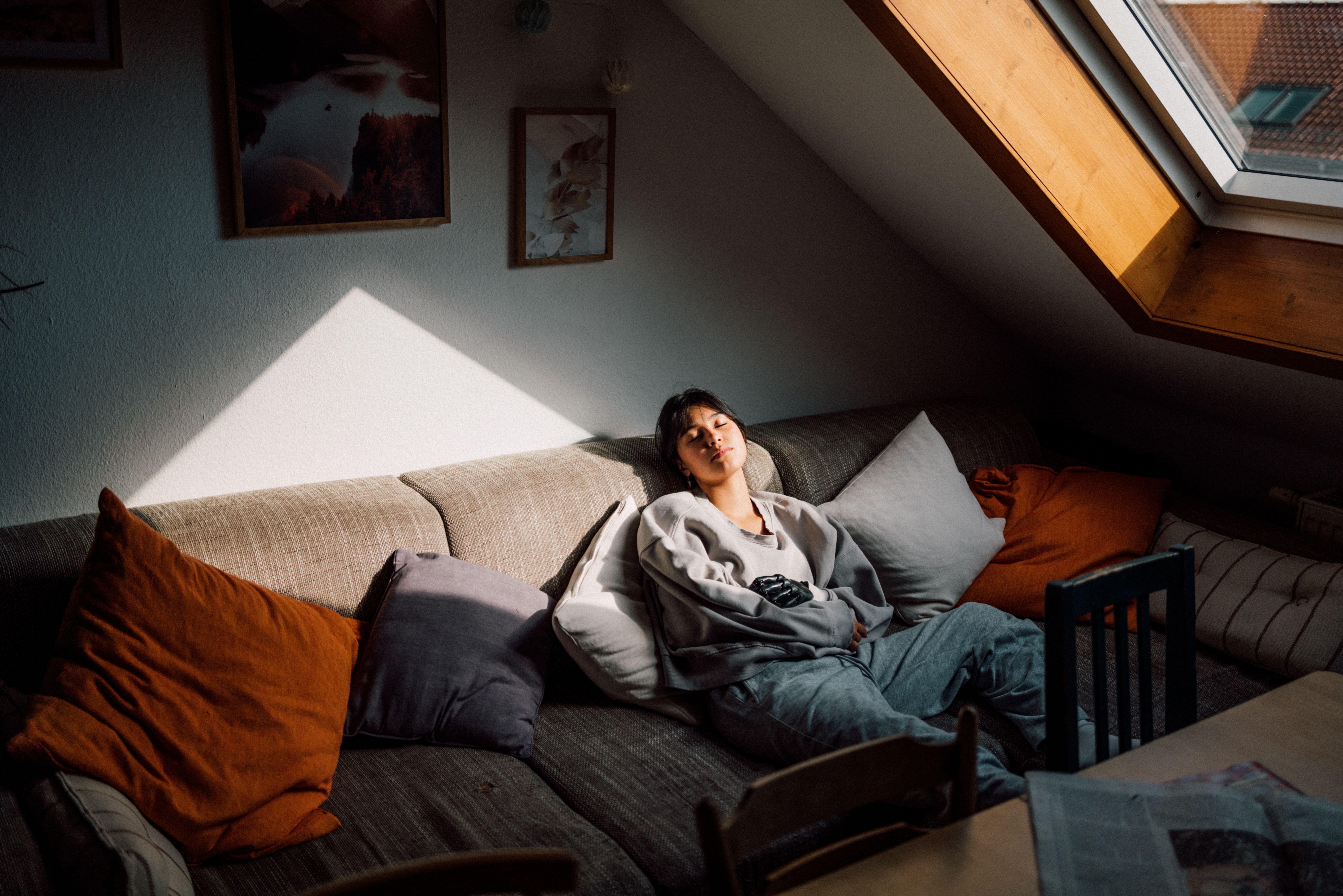 Junge Frau ruht entspannt auf einem Sofa, Sonnenlicht fällt durch ein Dachfenster ins Zimmer.